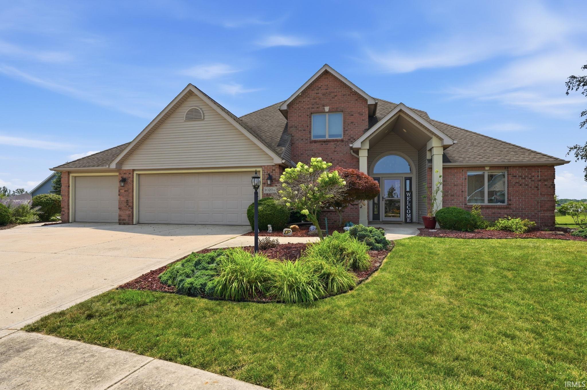 Brick-front exterior with a prominent arched entry, dual garage doors, and a concrete driveway