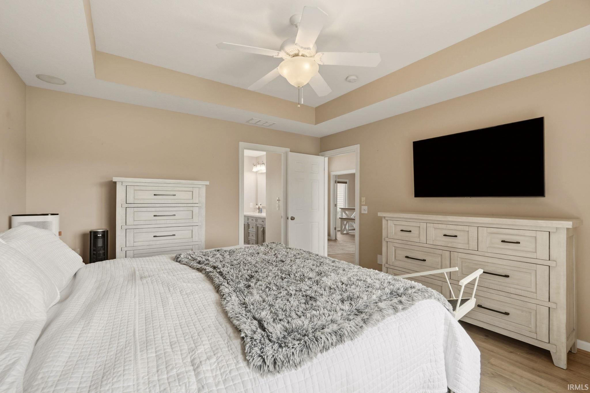 Bedroom with tray ceiling and recessed lighting, featuring wood-finish flooring and a ceiling fan