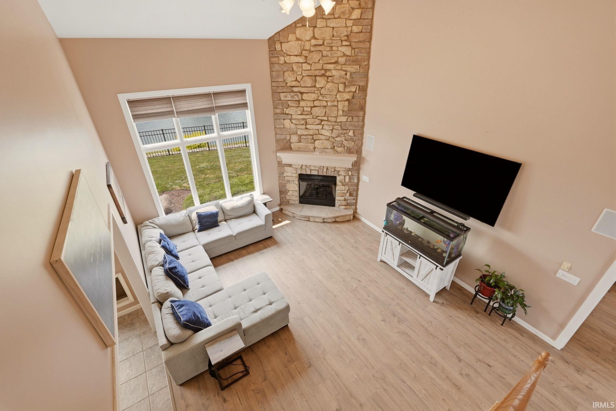 Two-story living area featuring a stone fireplace, wood-finish flooring, and a large picture window