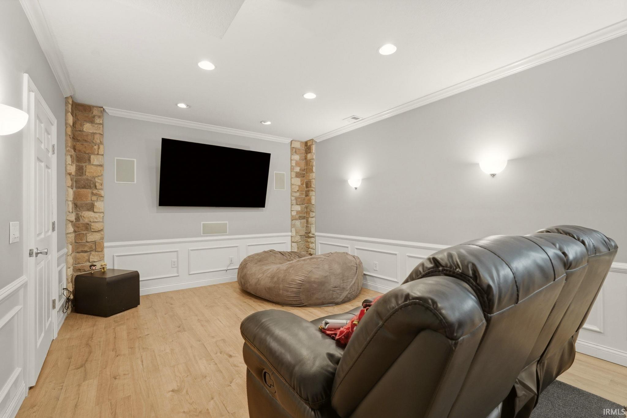 Media room featuring a wall-mounted display, built-in sound system, light wood-finish flooring, wainscoting, and recessed lighting