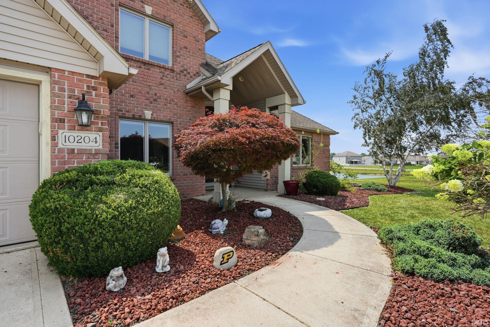 Brick exterior with a covered entry, featuring a concrete pathway, red mulch landscaping, and mature trees