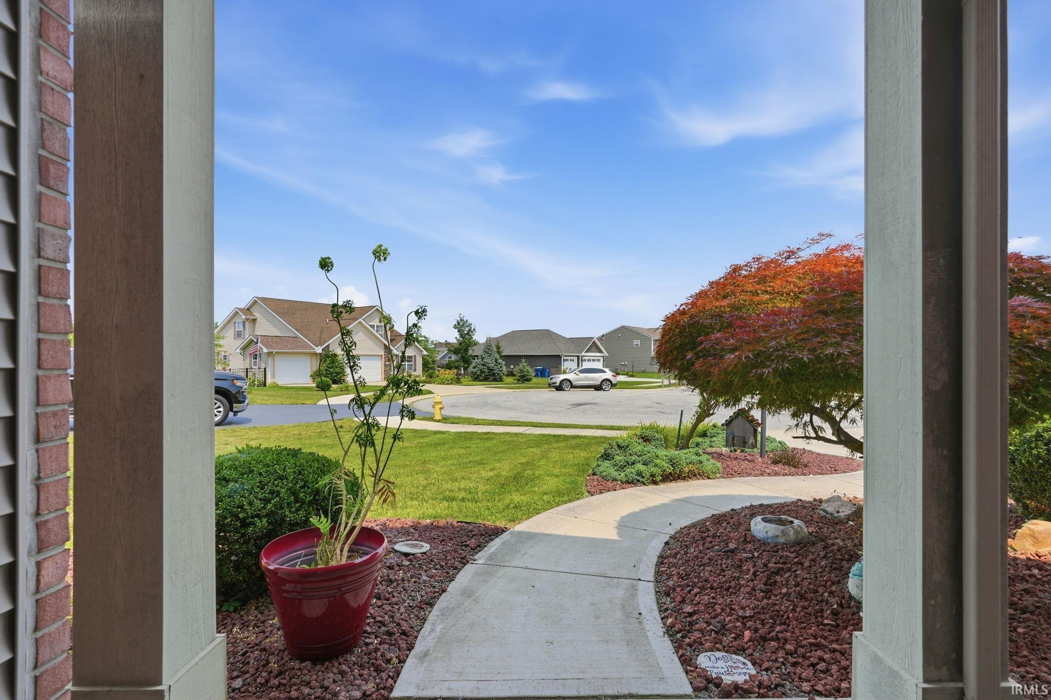 Inviting concrete walkway framed by landscaped beds with mature shrubs and a vibrant red-leafed tree