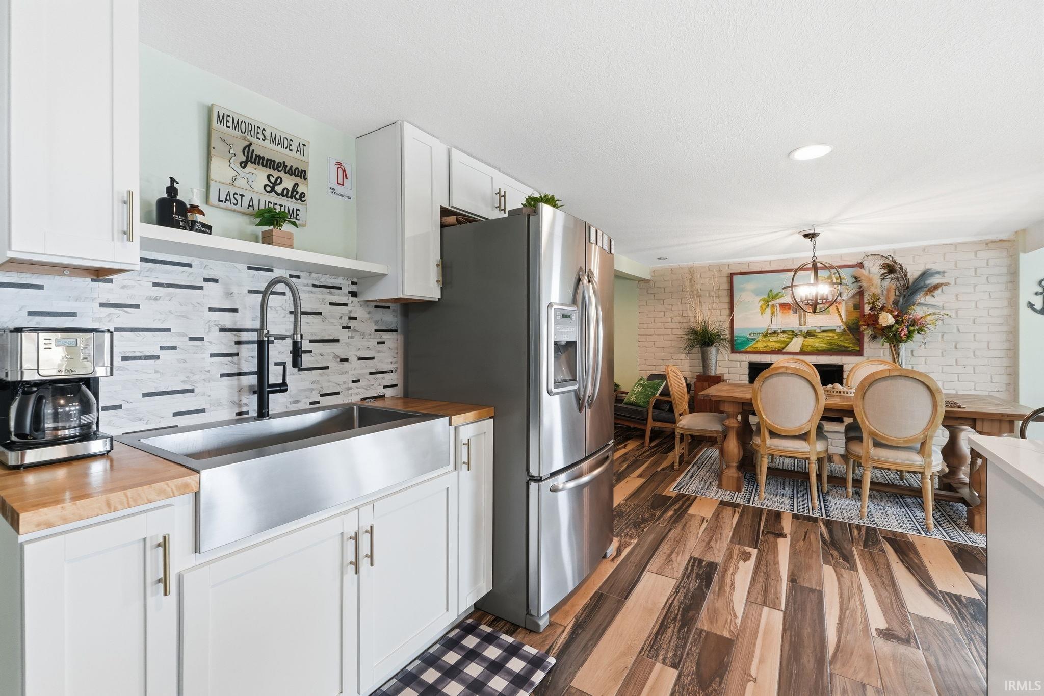 Open-concept kitchen and dining area featuring wood-finish flooring, white cabinetry with silver hardware, butcher block countertops, a stainless steel farmhouse sink, and a stainless steel refrigerator