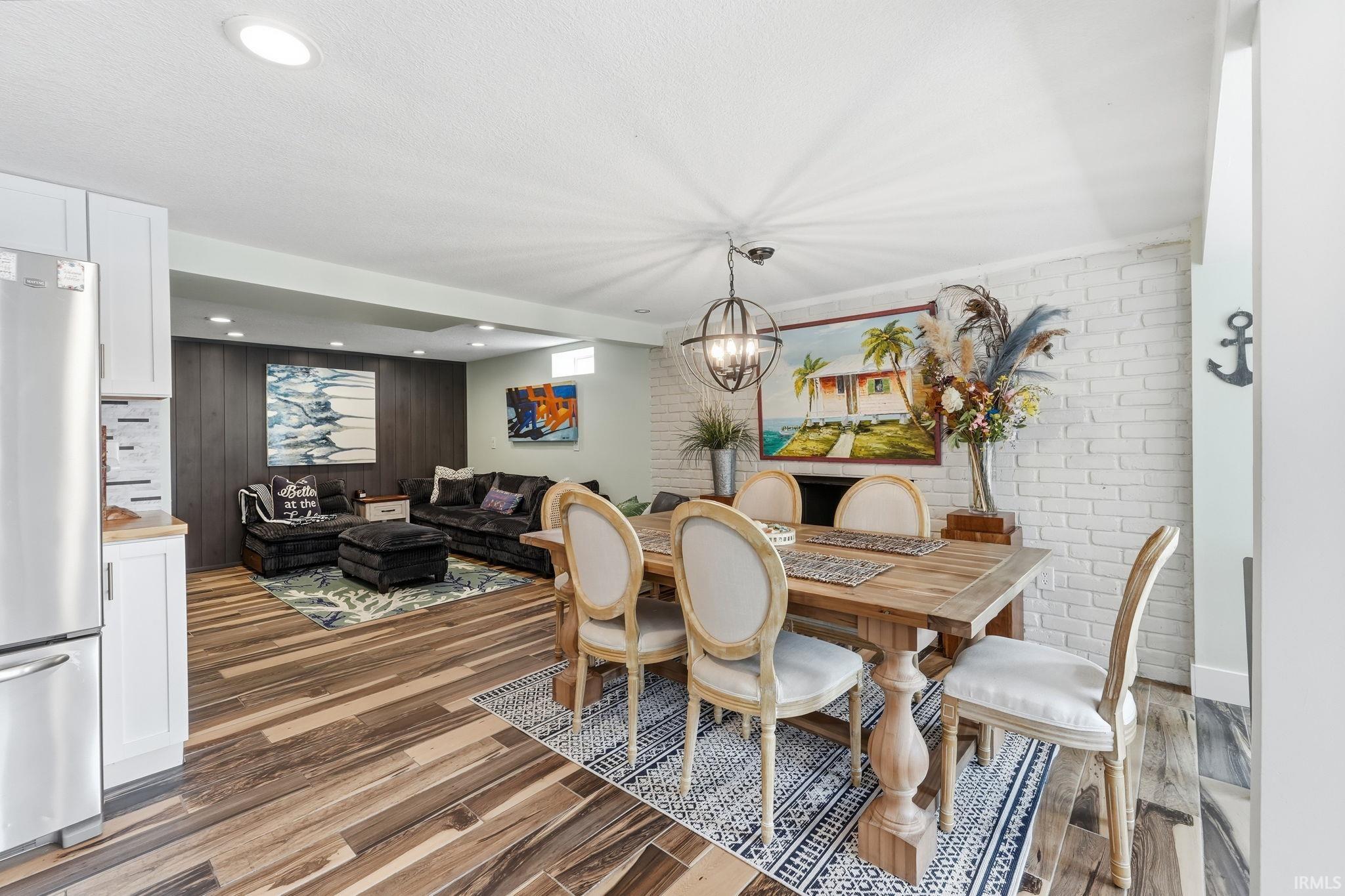 Open-concept dining and living area featuring wood-finish flooring, recessed lighting, and a white brick-finish accent wall