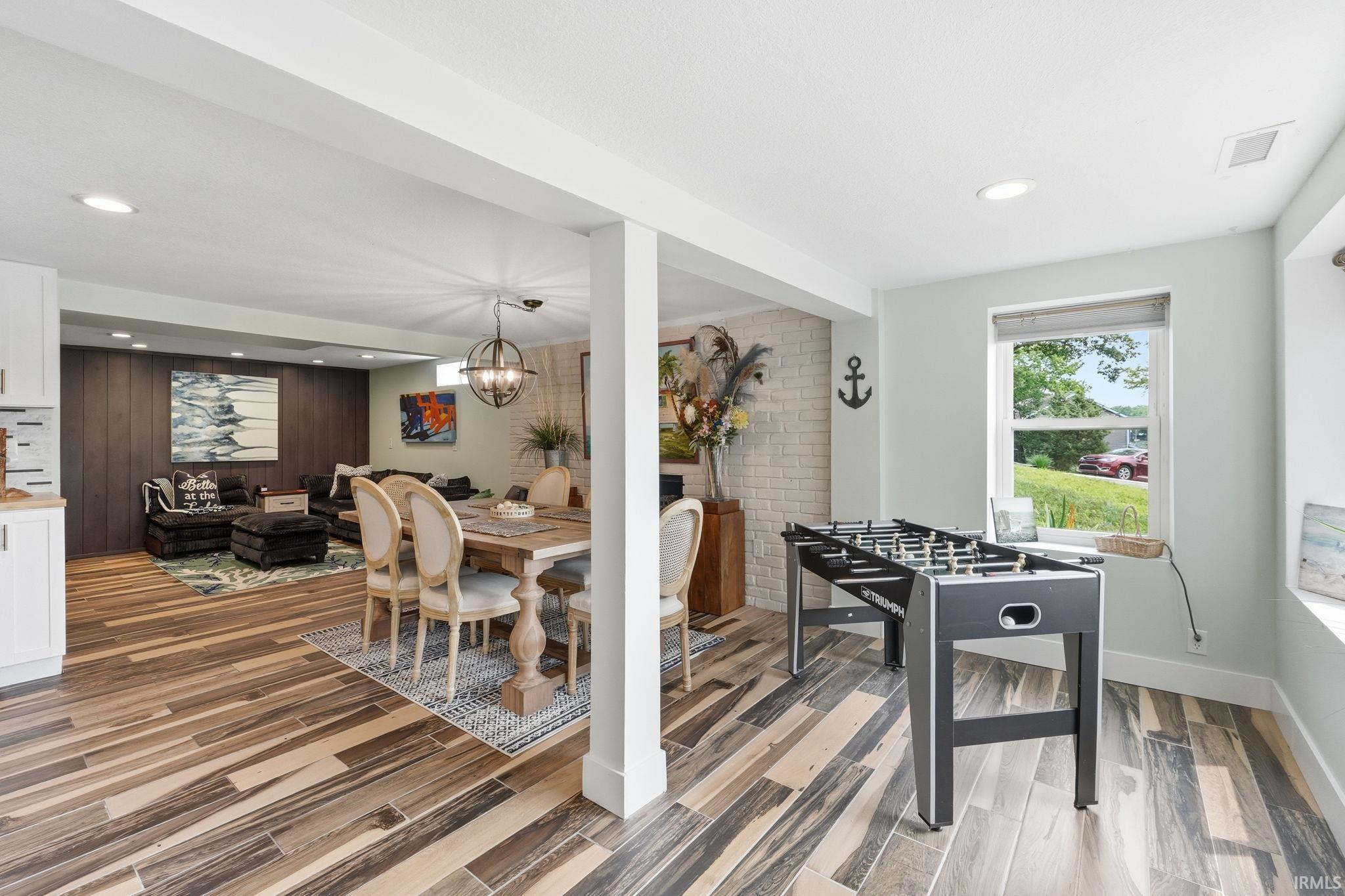 Finished lower level featuring wood-finish flooring, recessed lighting, a dining area with a chandelier, and a living area with a wood-paneled accent wall