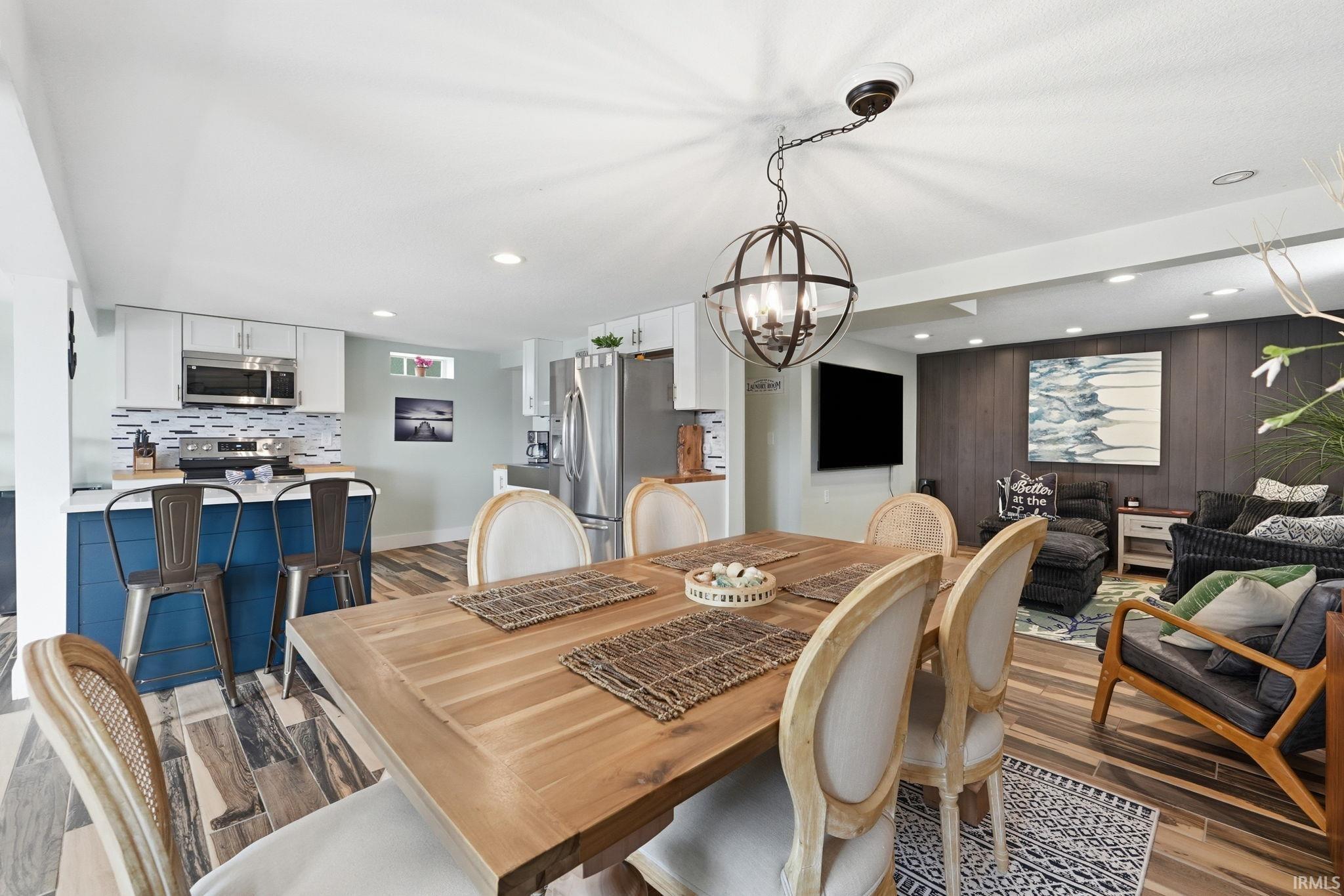 Open-concept living space featuring wood-finish flooring, a contemporary dining chandelier, and recessed lighting