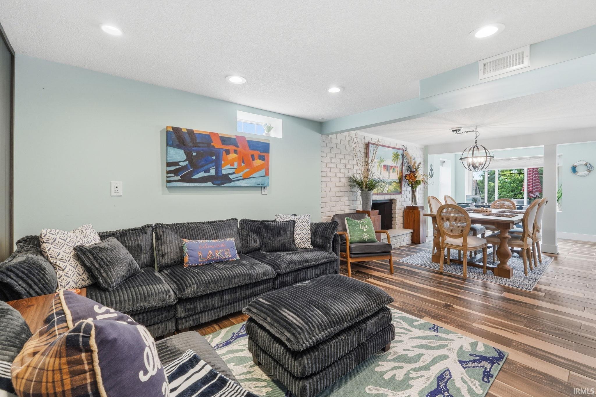 Open-concept living area featuring wood-finish flooring, recessed lighting, and a white brick fireplace