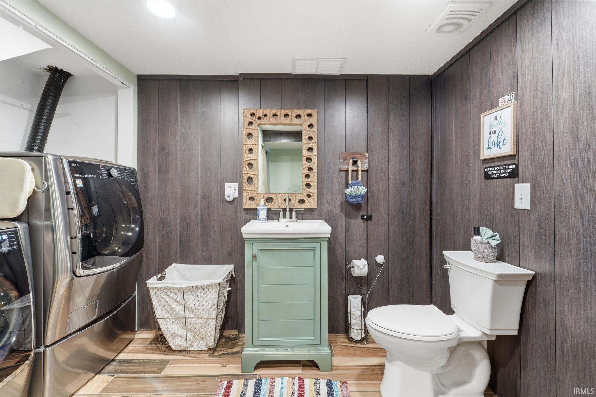 Powder room featuring wood-finish flooring, vertical wood-panel wall treatment, and a green vanity with an integrated sink