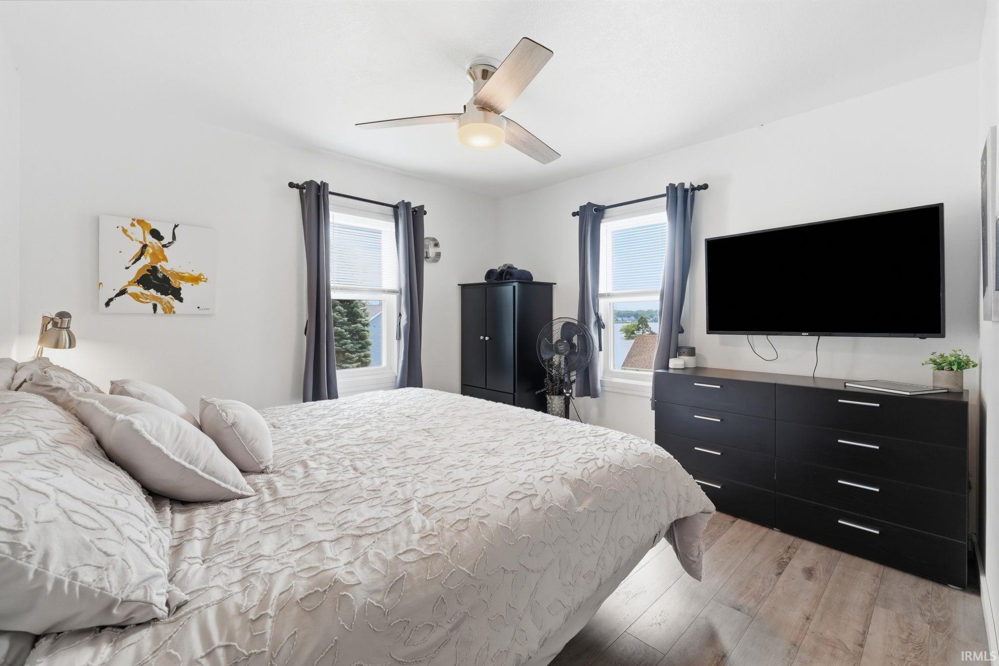 Bedroom featuring wood-finish flooring, two windows, and a ceiling fan with integrated lighting