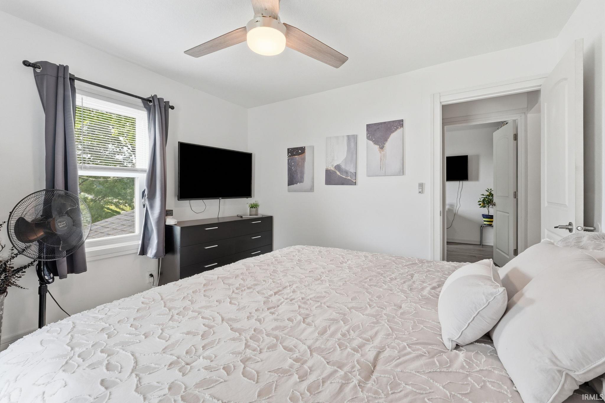 Bright bedroom featuring a ceiling fan with integrated lighting, a double-hung window, and a white paneled door