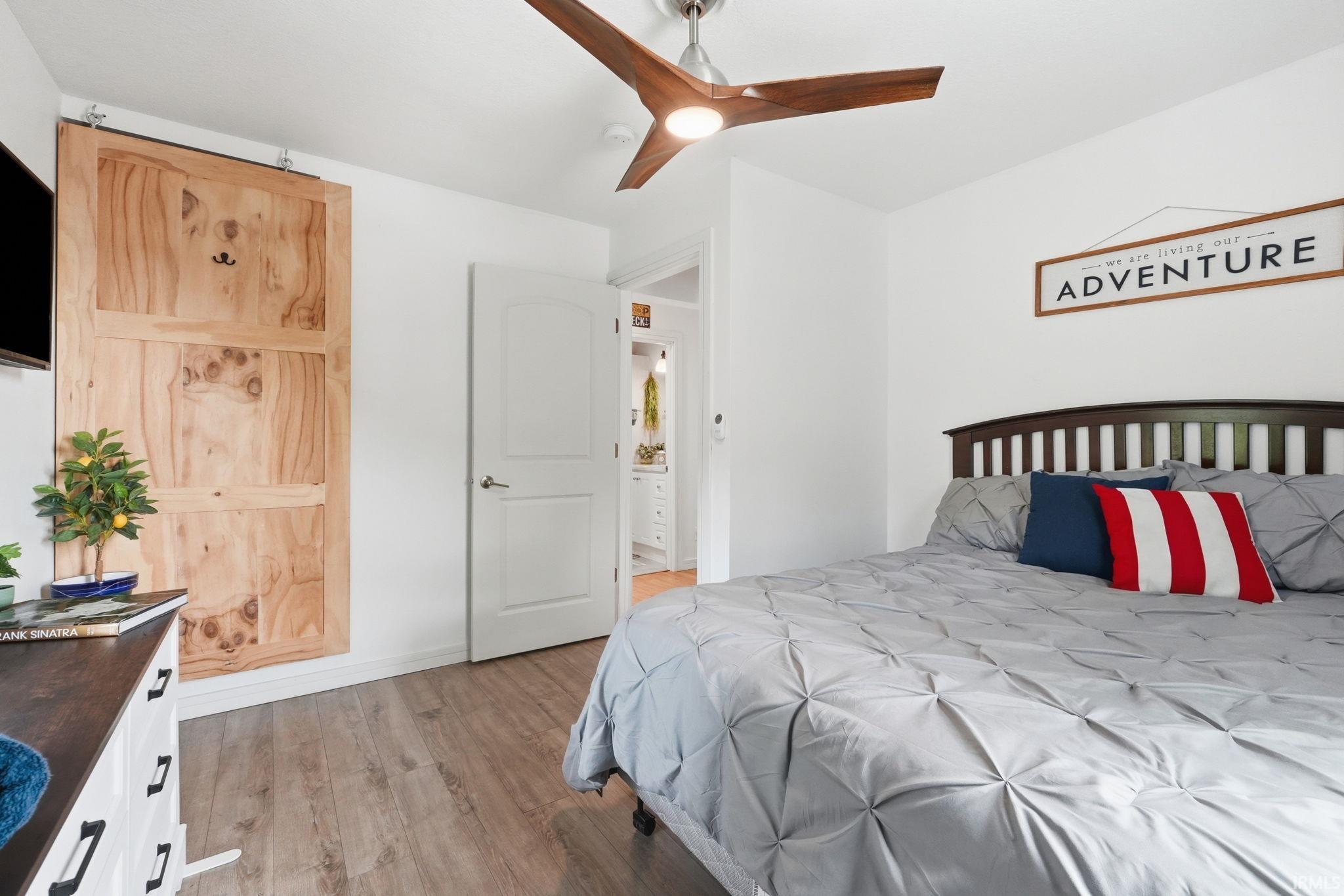 Room featuring wood-finish flooring, a contemporary ceiling fan with integrated lighting, and a barn-style sliding door