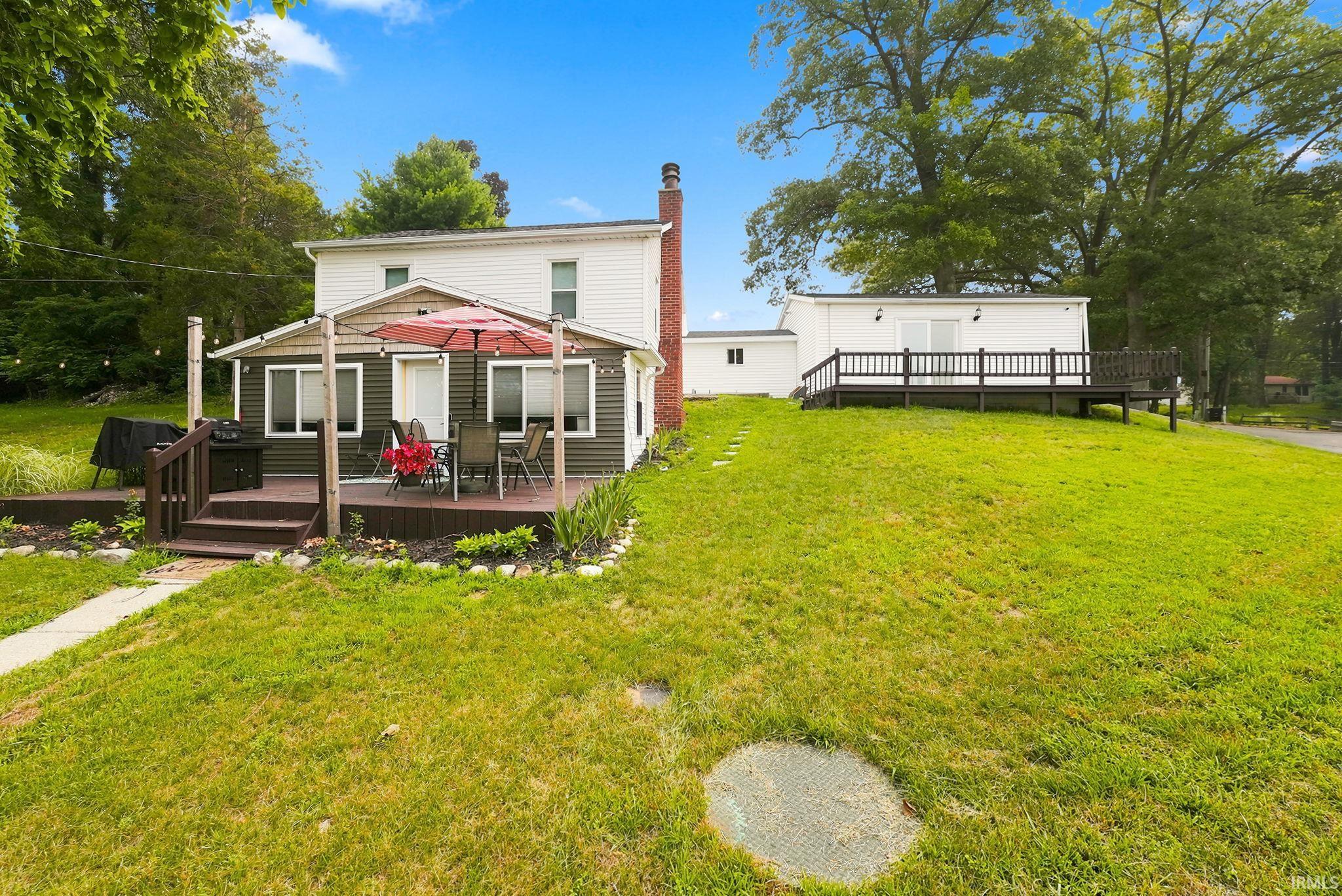Two-story residence with white siding and a brick chimney, featuring a spacious rear deck with steps