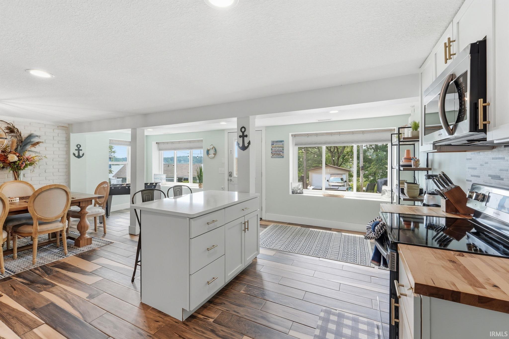 Open-concept kitchen and dining area featuring wood-finish flooring, recessed lighting, a white kitchen island with a light-colored countertop, and a white brick-finish accent wall