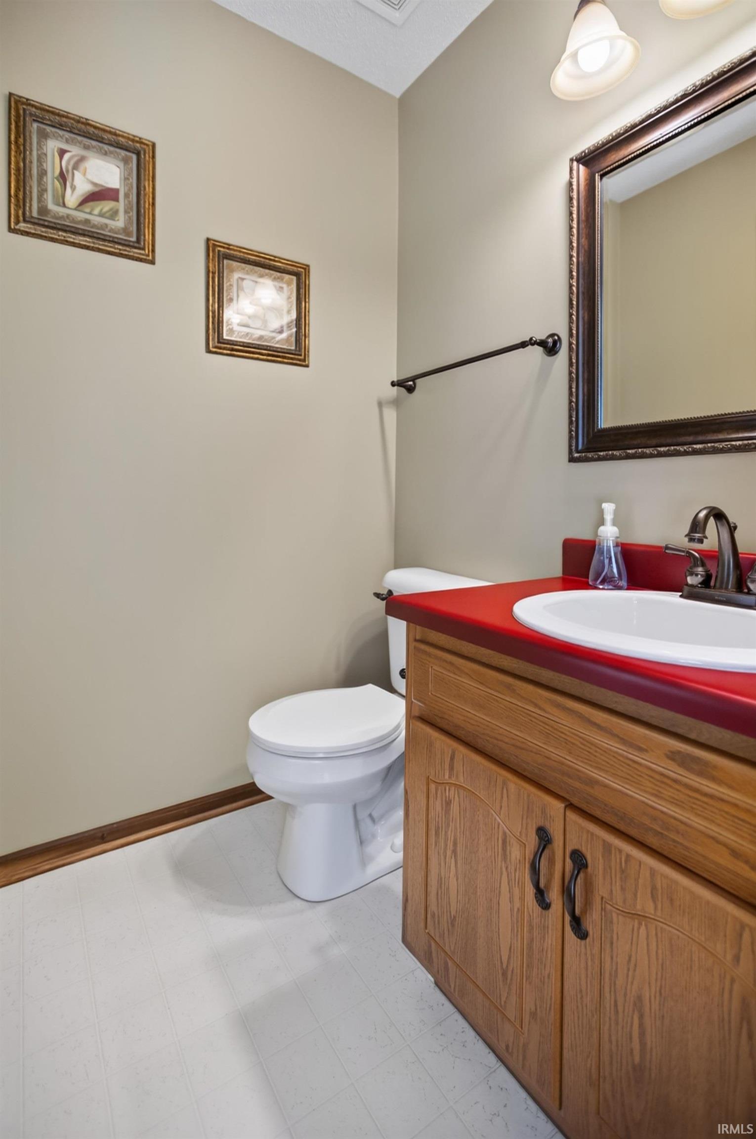 Bathroom vanity with a red countertop, white basin, and wood-finish cabinetry