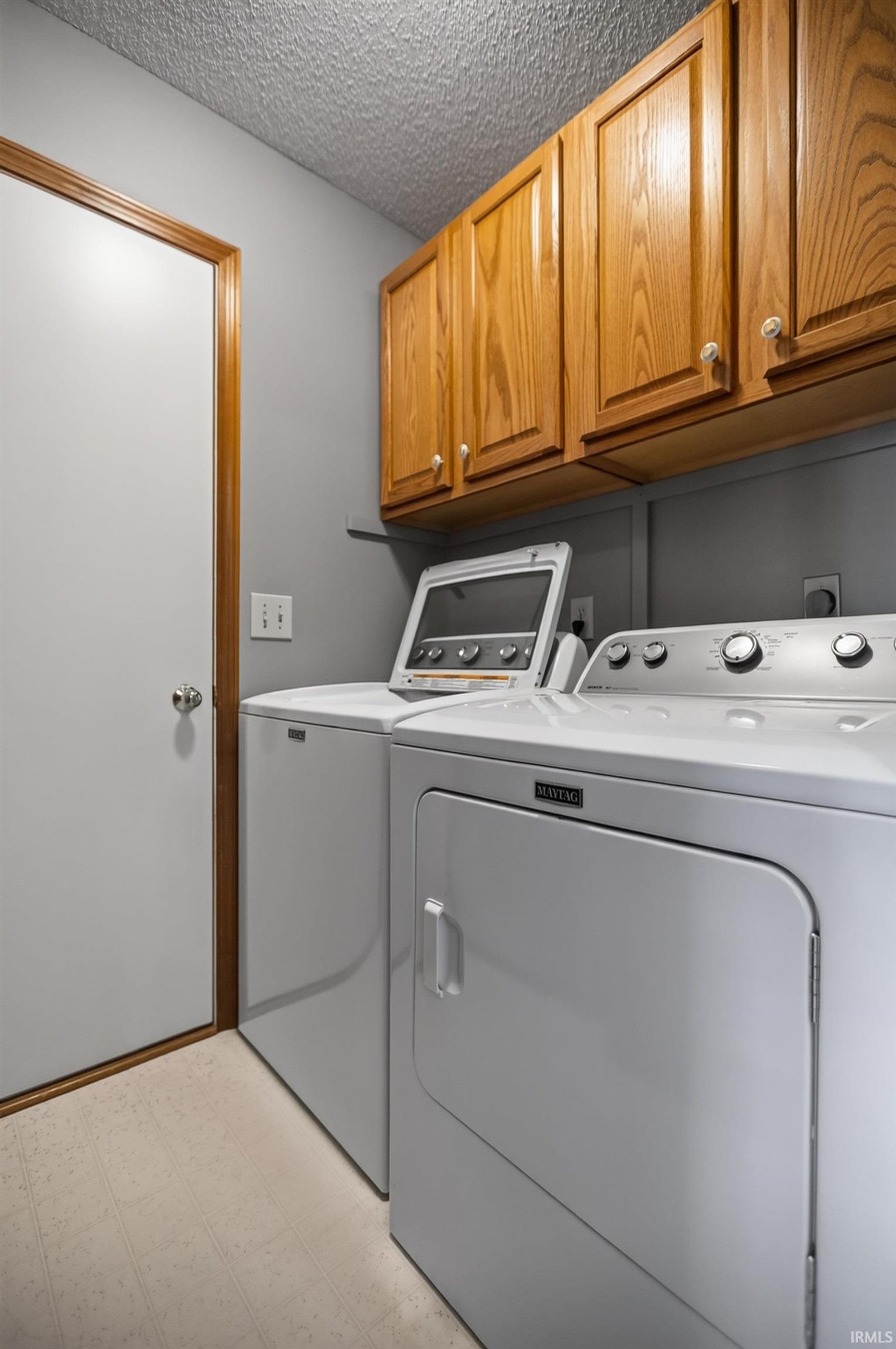 Laundry area featuring overhead wood cabinetry, a top-loading washing machine, and a front-loading dryer