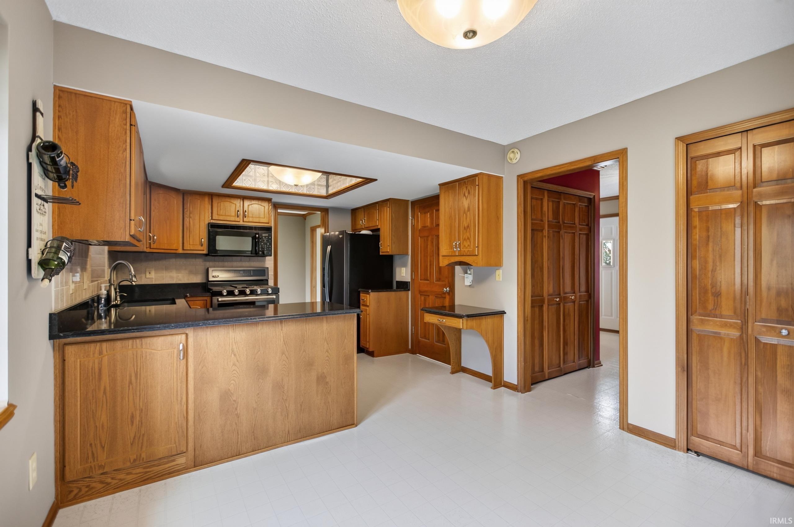 Kitchen featuring wood cabinetry, black countertops, and a full suite of black and stainless steel appliances