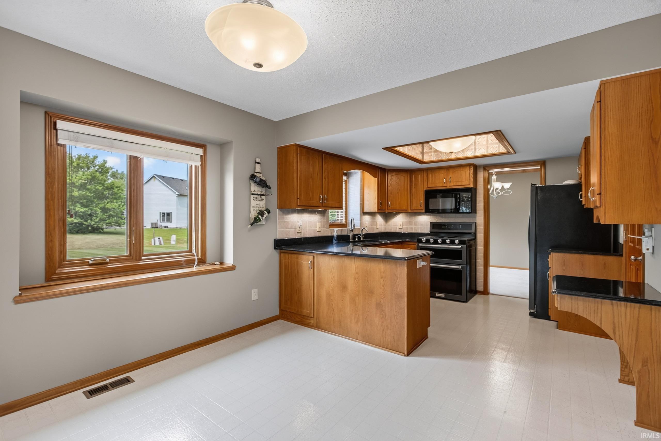 Kitchen featuring wood cabinetry, black appliances, dark countertops, and light flooring