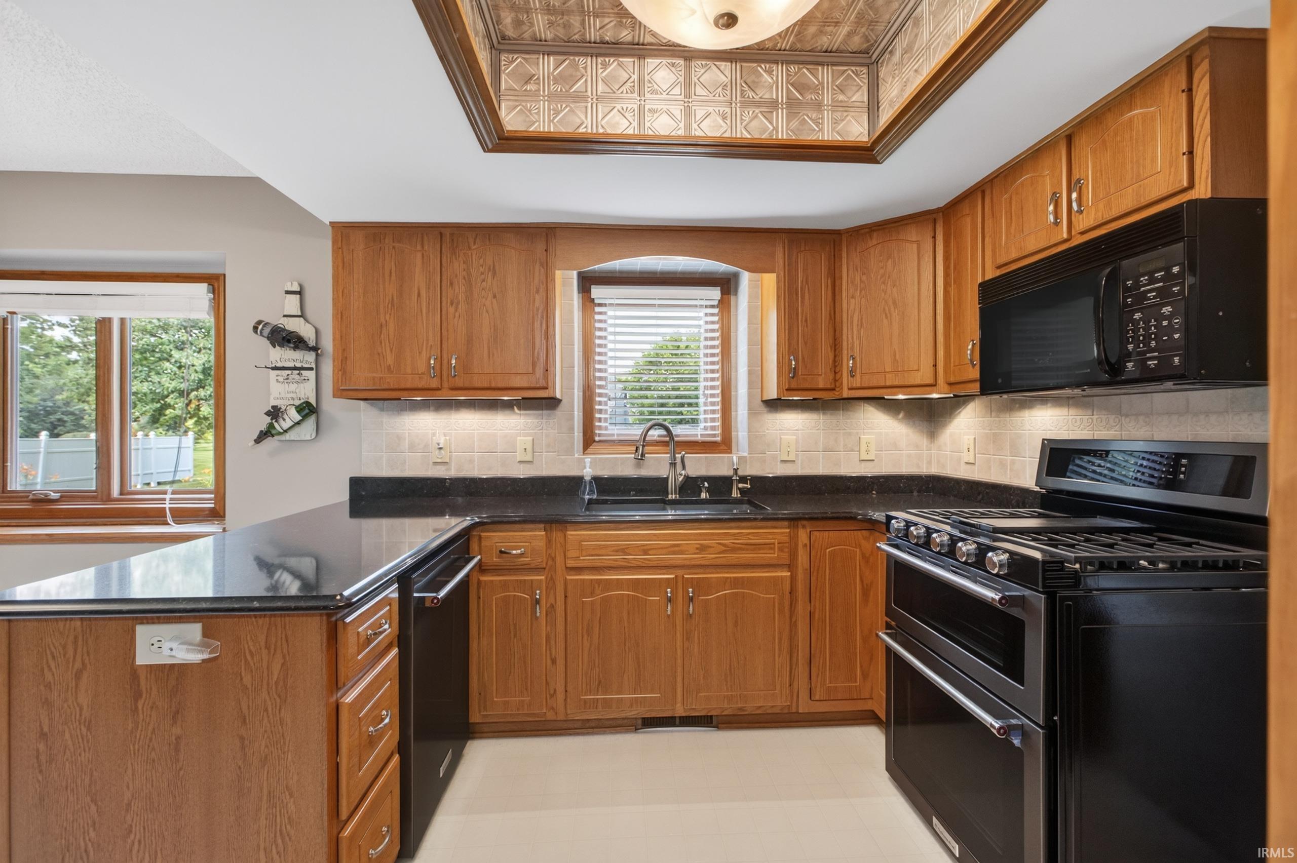 Kitchen featuring wood cabinetry, black countertops, undermount sink, and black appliances