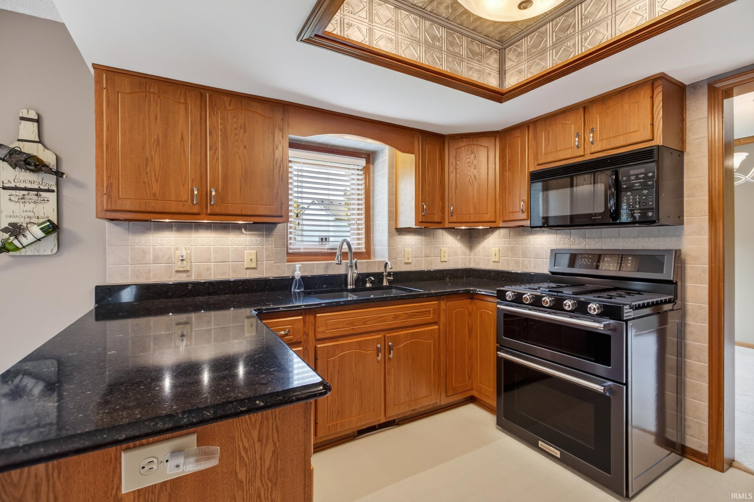 Kitchen featuring wood cabinetry, dark countertops, tiled backsplash, and stainless steel double oven range