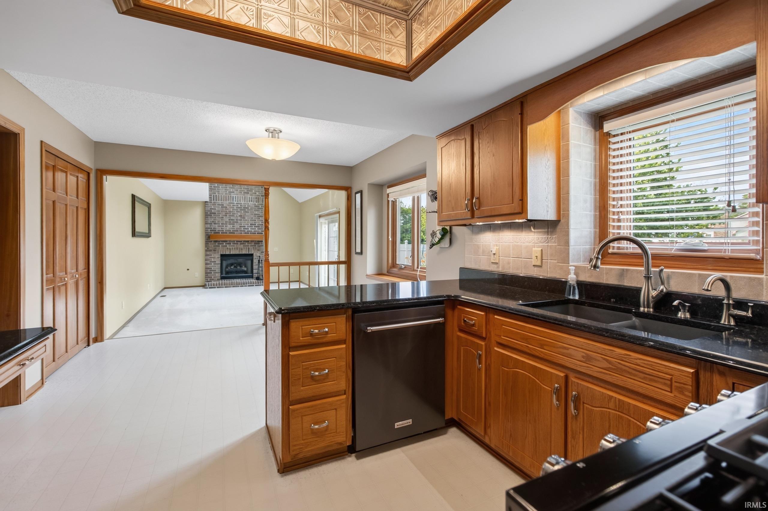 Kitchen featuring wood cabinetry, black countertops, undermount sink, and stainless steel dishwasher