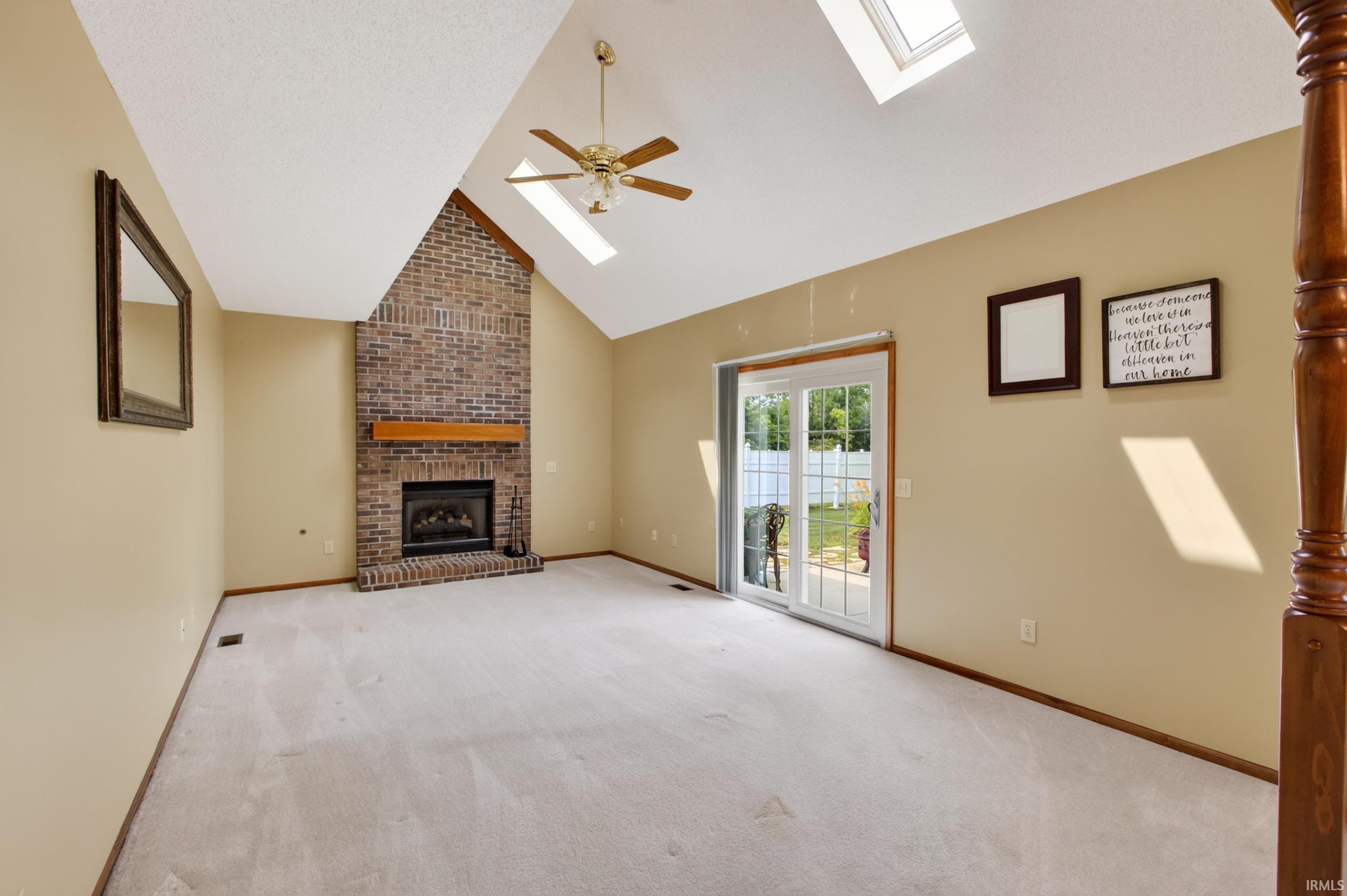 Living area featuring a brick fireplace with a wood mantle, vaulted ceilings, and two skylights