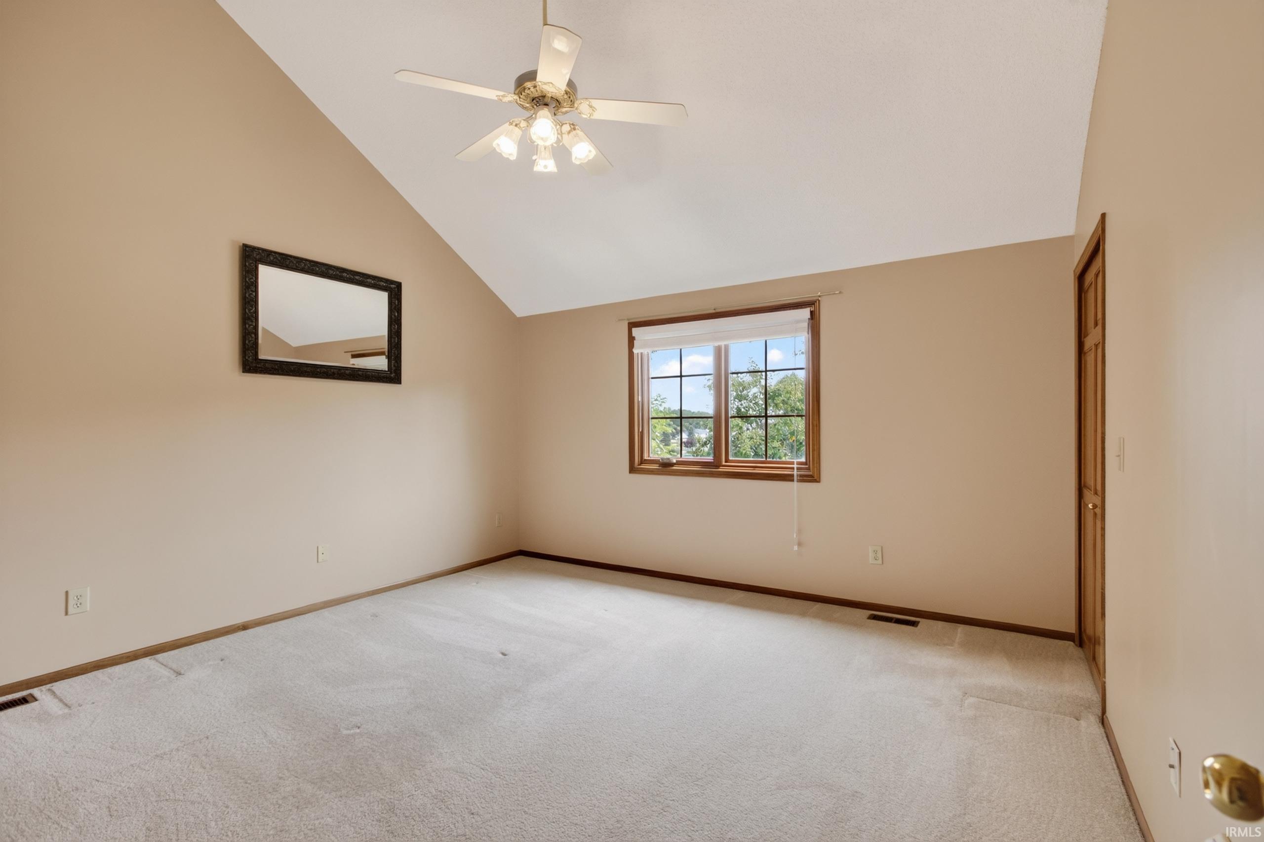 Room with vaulted ceiling, light beige walls, and light-colored carpeting