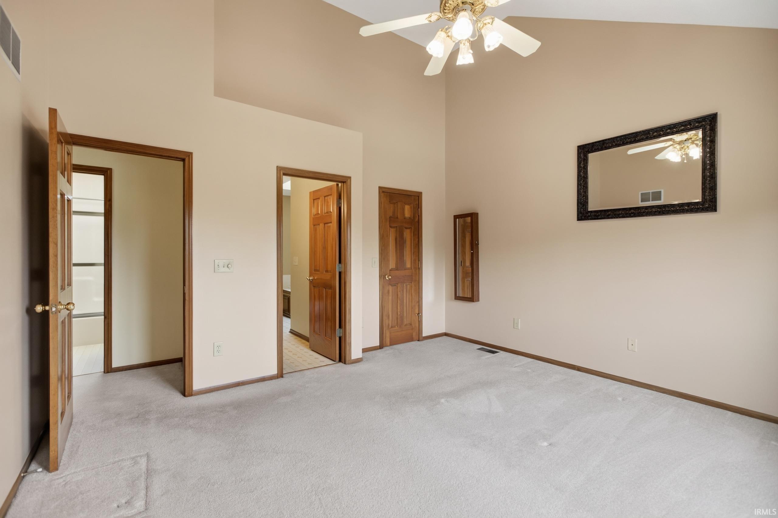 Spacious room featuring vaulted ceilings, light-colored carpeting, and wood-finish doors with matching trim