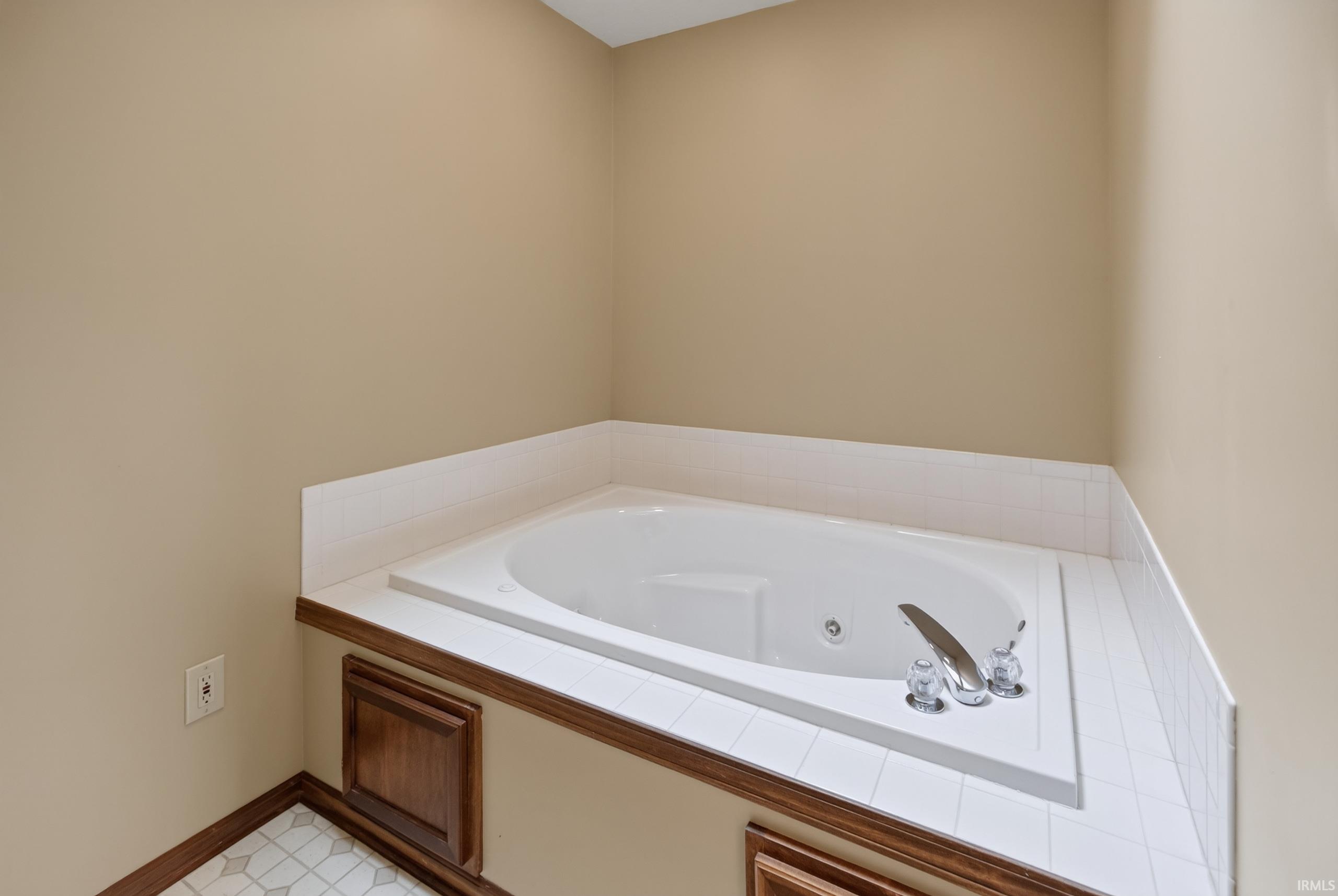 Built-in soaking tub with a tiled surround, wood-finish trim, and polished chrome fixtures
