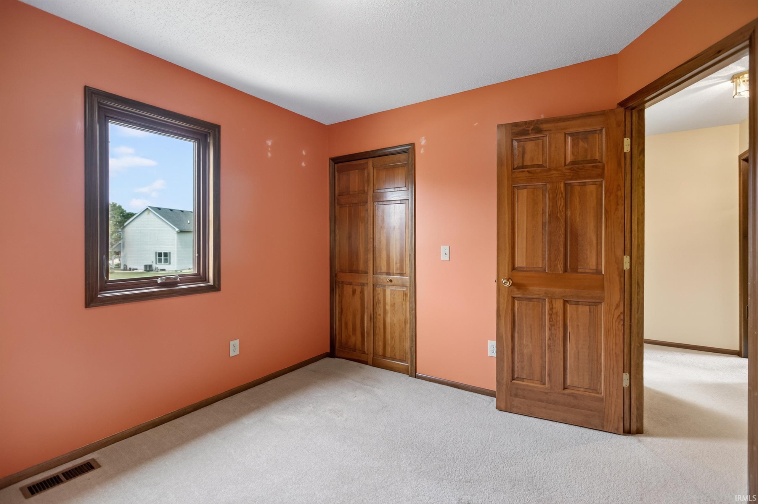 Carpeted room featuring a single window with dark wood trim, two solid wood doors, and one wood bi-fold closet door