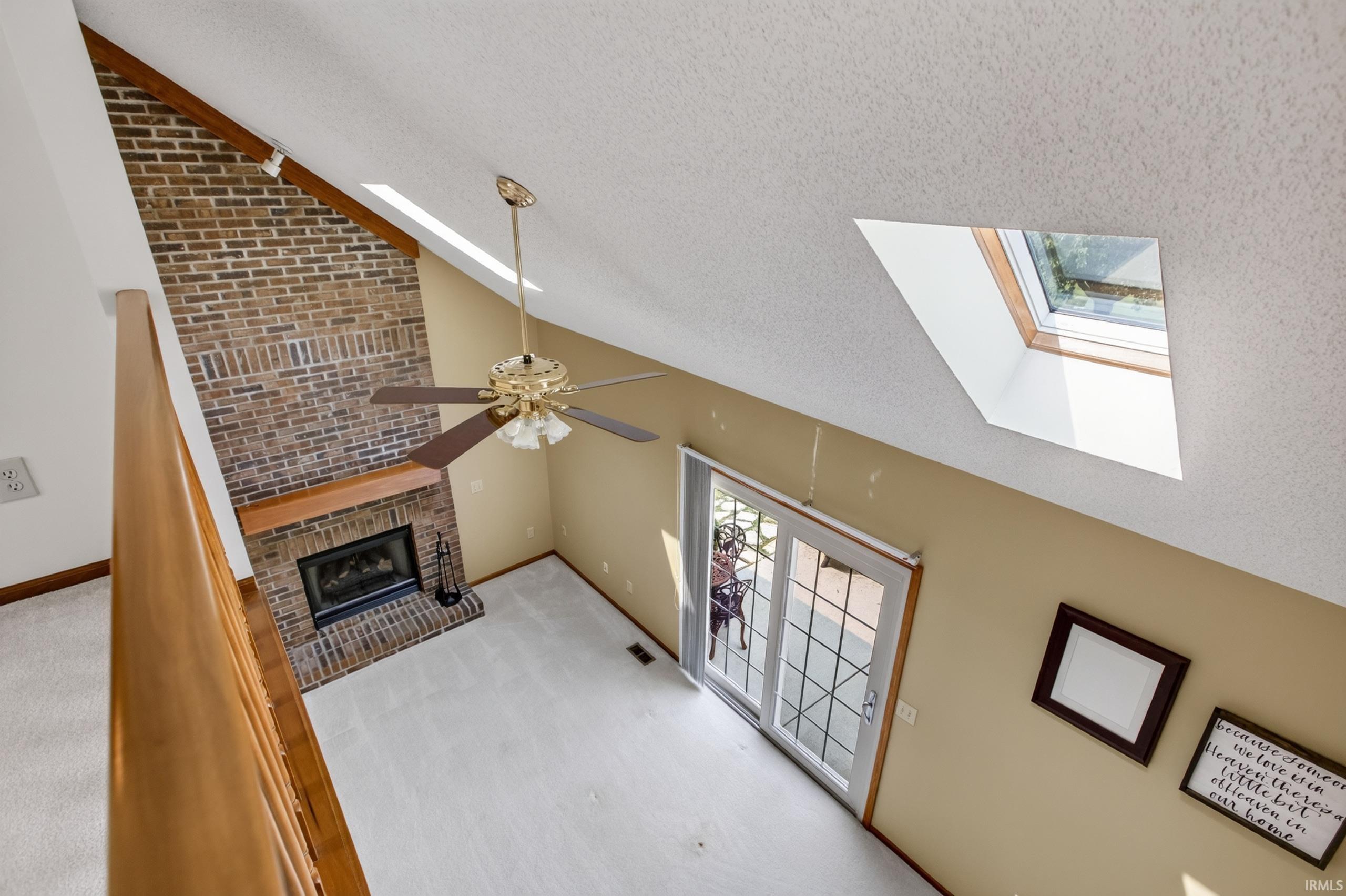 Vaulted ceiling great room featuring a brick-face fireplace with wood mantel, a ceiling fan, and a skylight