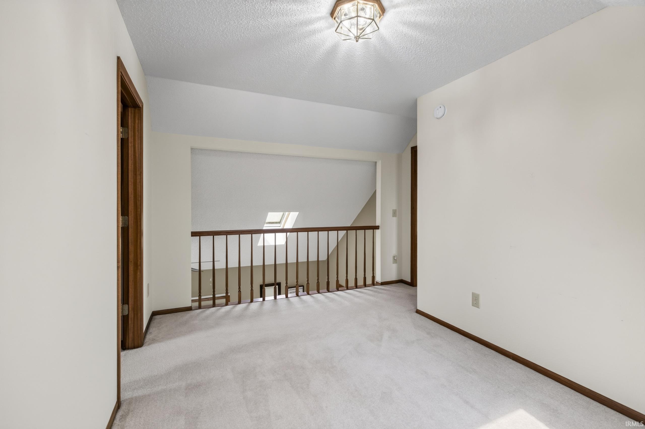 Carpeted landing with a wood-stained railing, recessed open wall, and an overhead light fixture