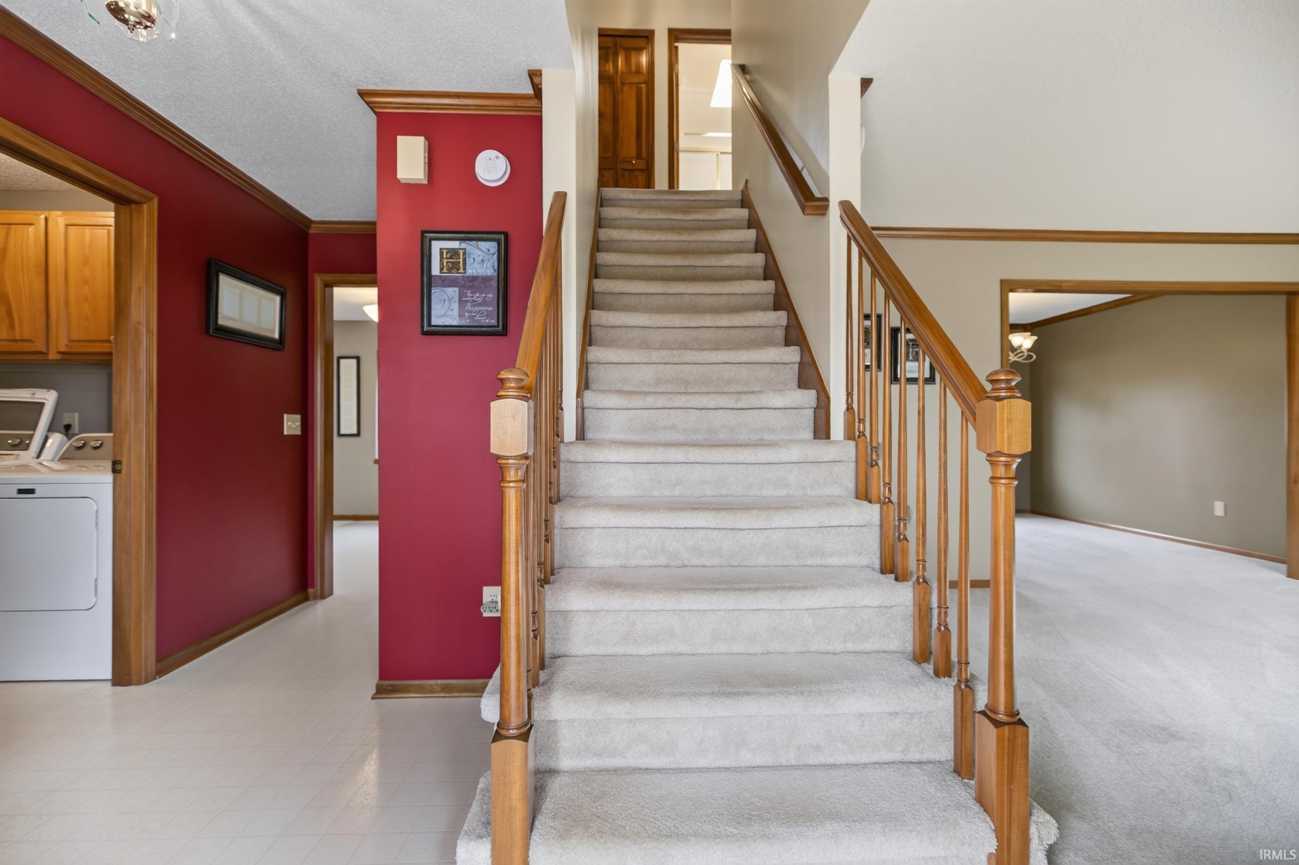 Carpeted staircase with wood handrails, flanked by a two-story entryway and a hallway with a laundry area