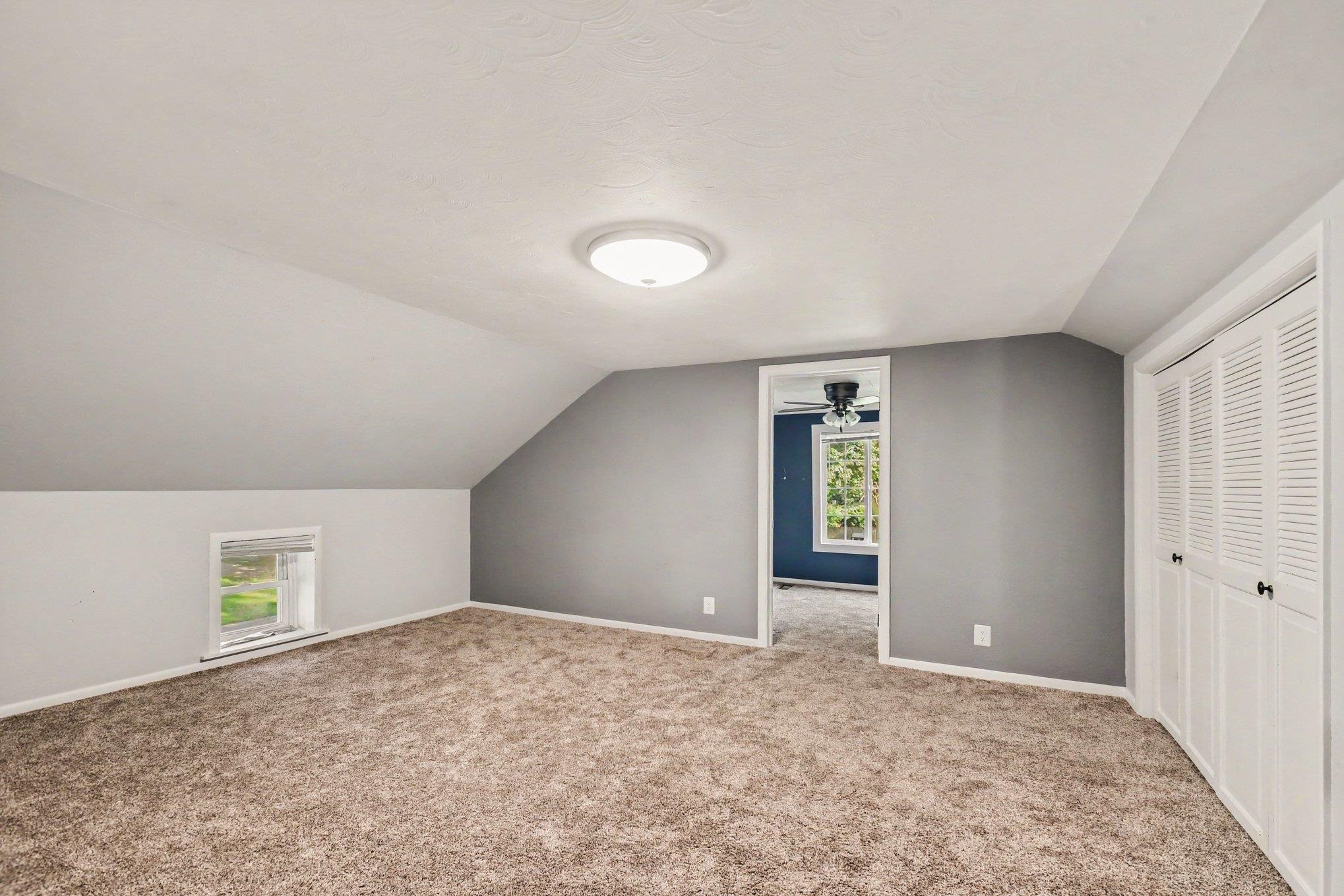 Carpeted room featuring sloped ceilings, a recessed window, and white louvered bifold closet doors