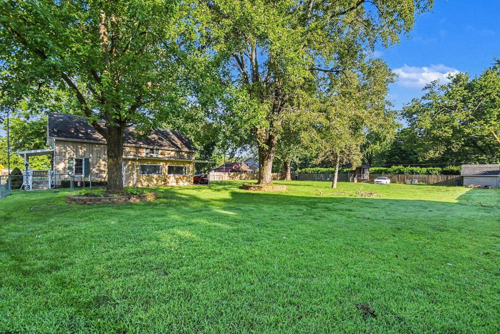 Expansive grassy yard with mature trees, a wooden outbuilding, and a partial privacy fence