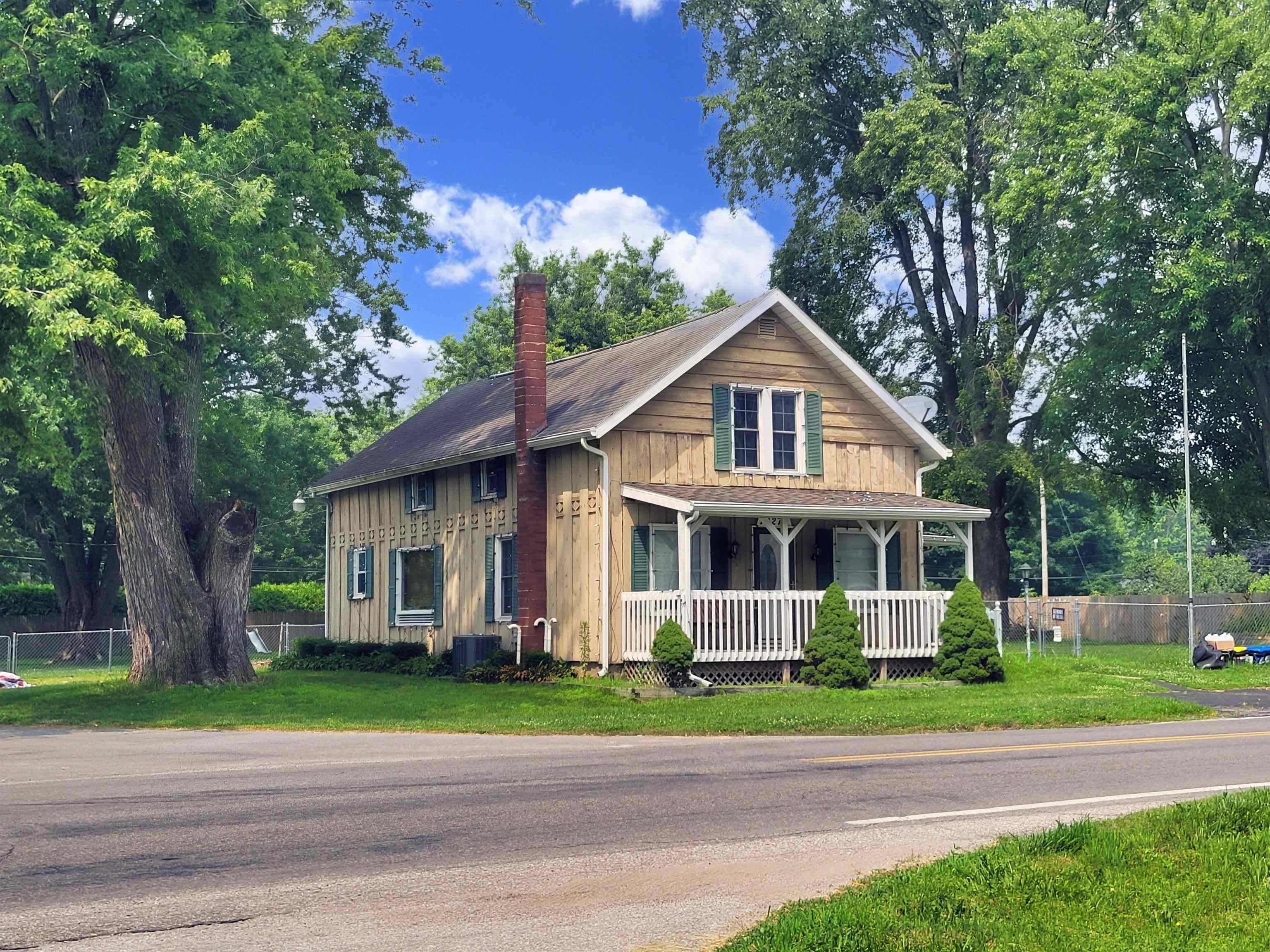 Two-story home featuring natural wood-finish siding, a covered front porch with white railing, and an exterior brick chimney