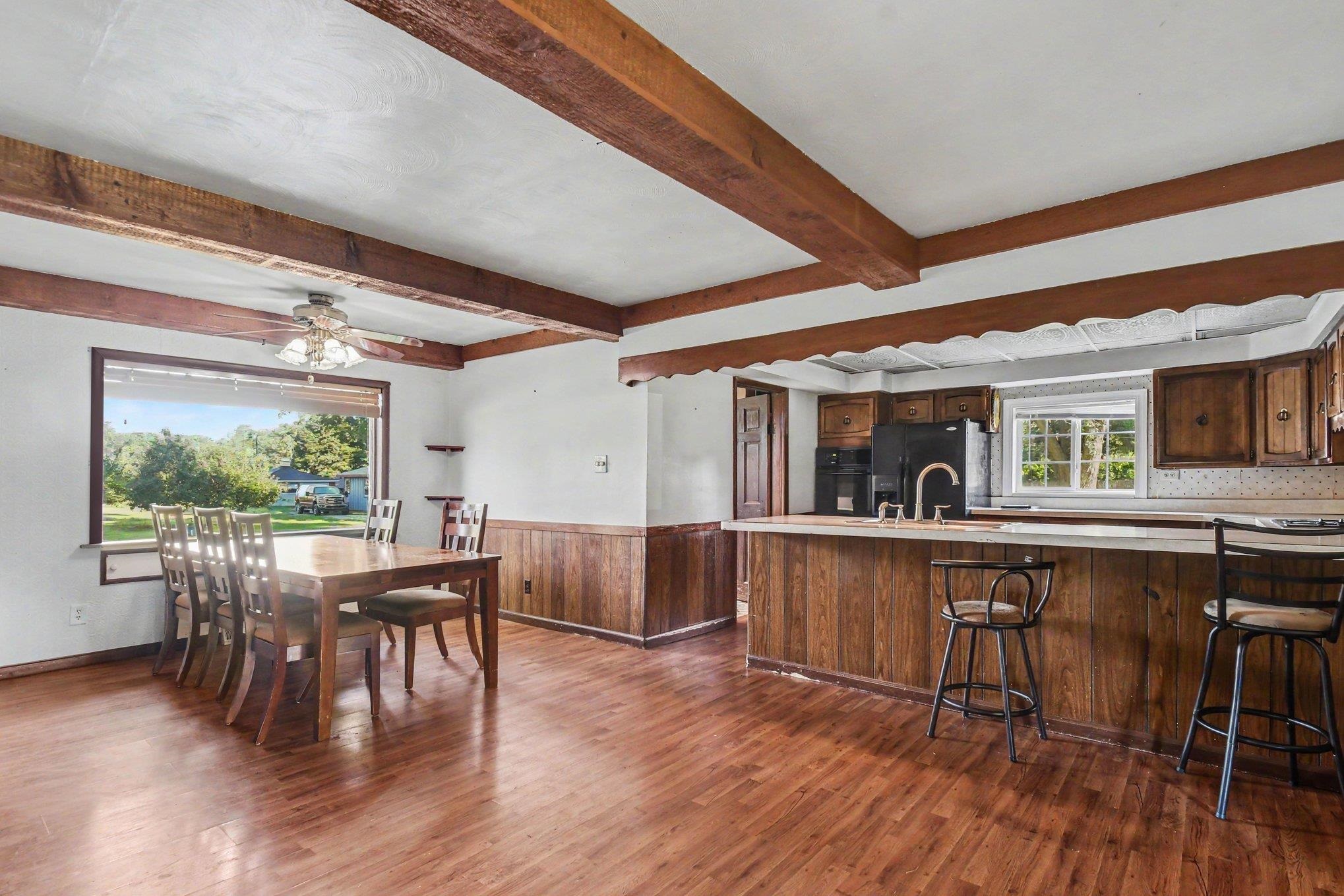 Exposed ceiling beams, wood-finish flooring, wood paneling, kitchen island, and built-in cabinetry