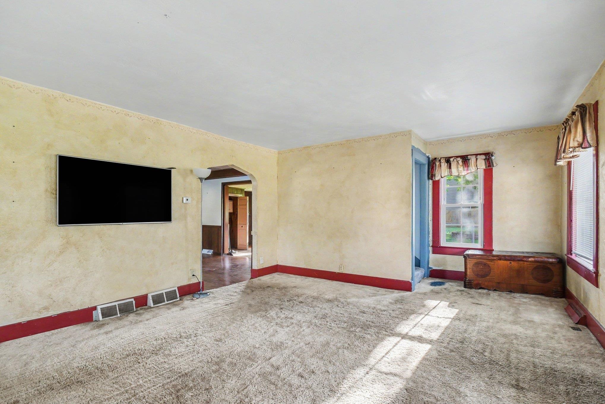 Arched doorway providing access to additional spaces, window with red trim, and wall-mounted television bracket