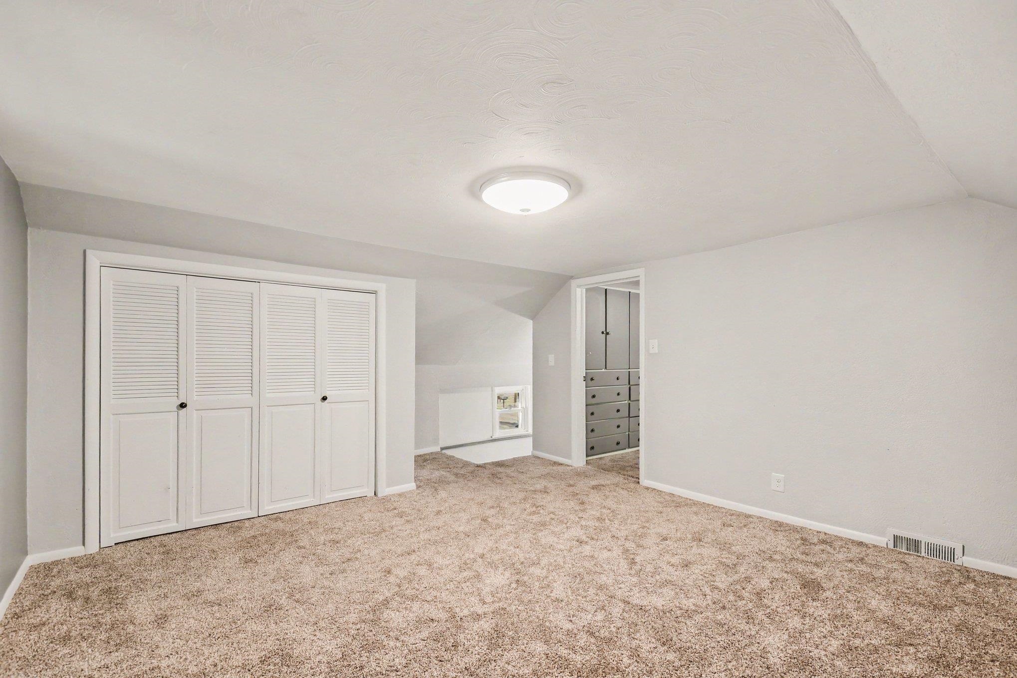 Carpeted flooring, white louvered bifold closet doors, flush-mount ceiling light, and built-in cabinetry
