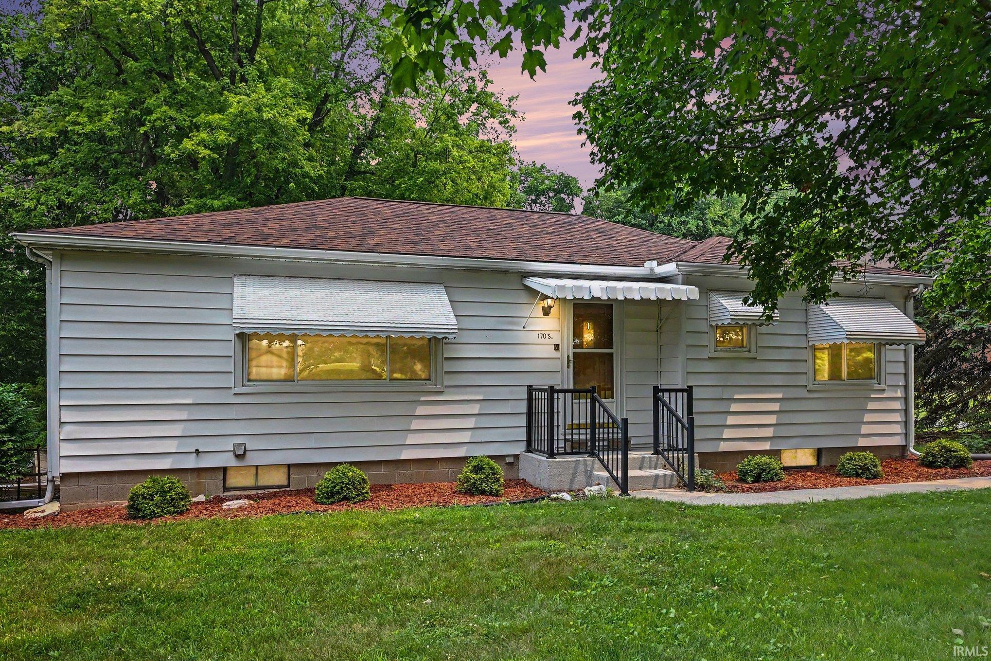 Single-story residence featuring light-toned siding, a brown shingle roof, and a front entry with black metal railings