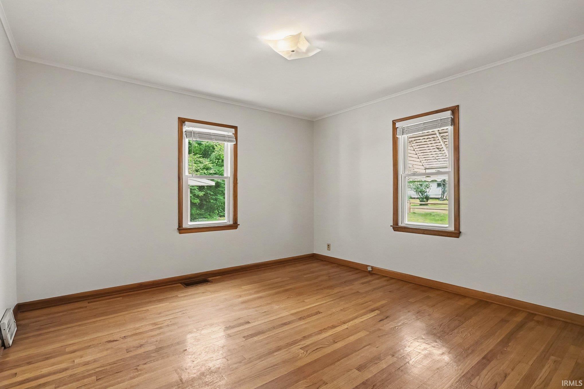 Hardwood flooring throughout this room, featuring two windows with wood trim and white blinds