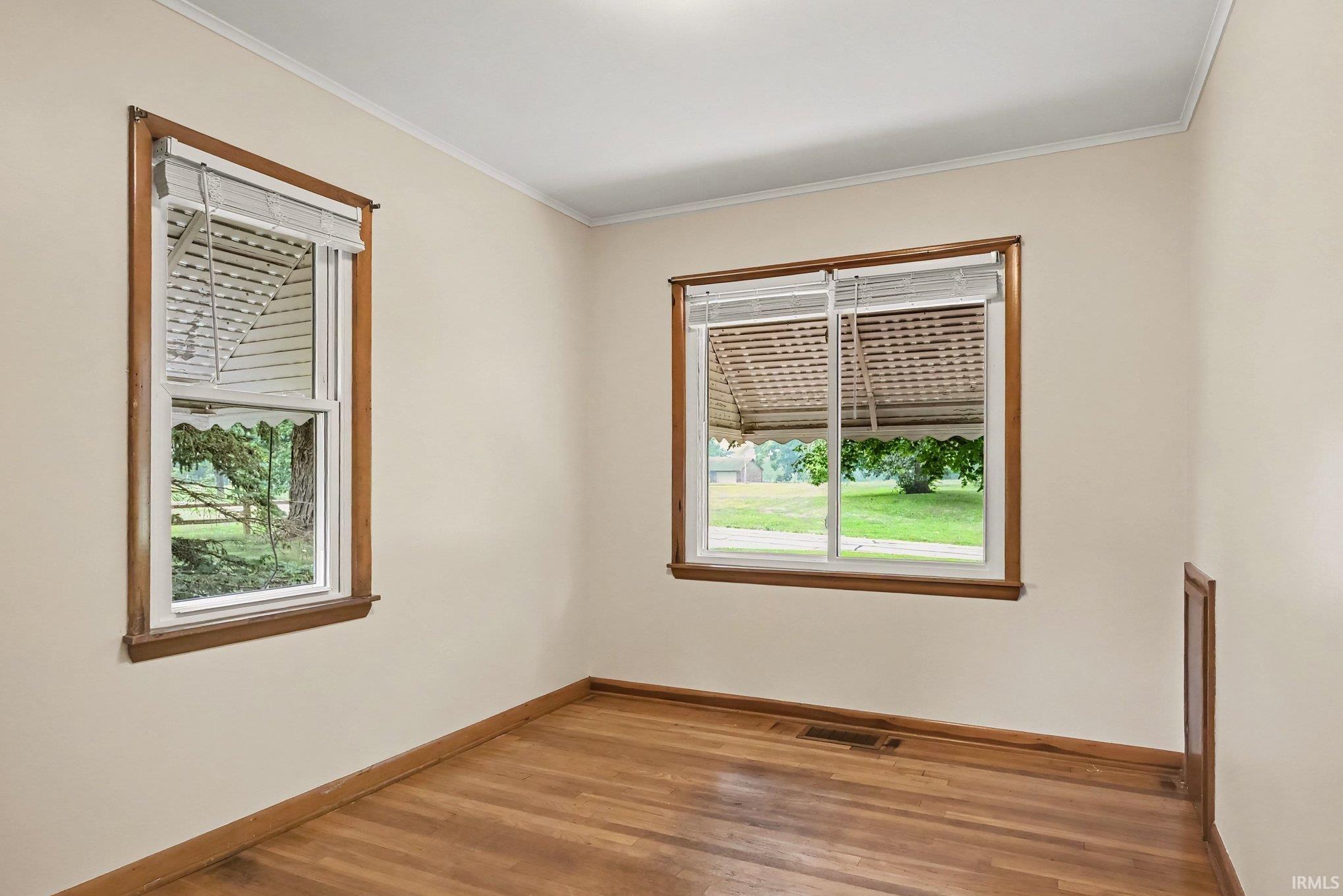 Hardwood flooring spans this room featuring two windows with wood-trim framing, offering natural light