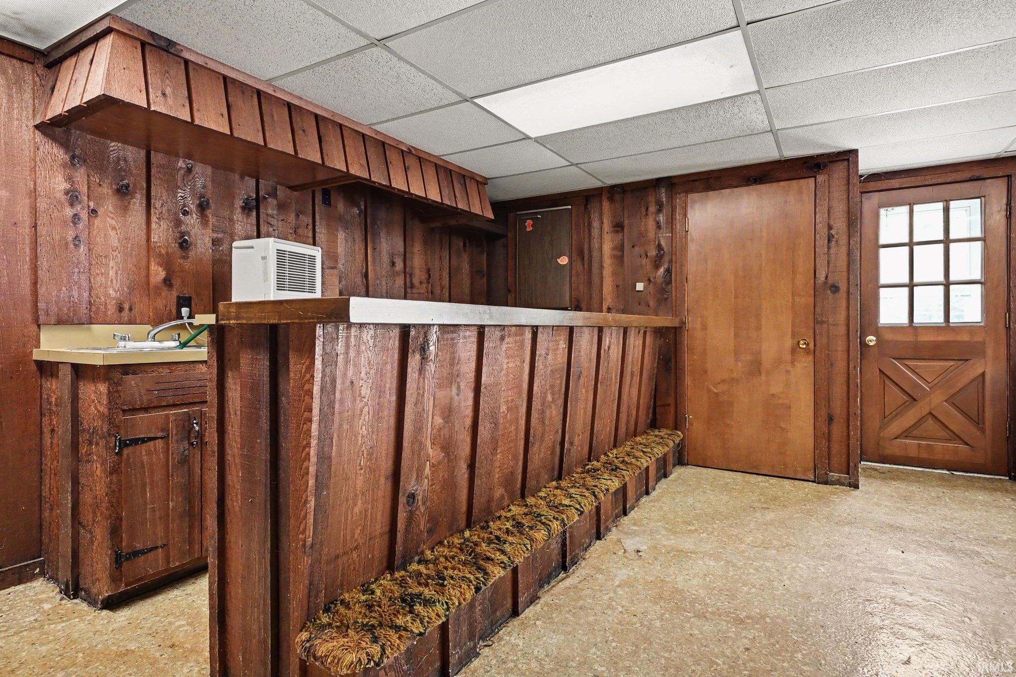 Recreation room featuring wood-paneled walls, a built-in wet bar with a countertop, and integrated seating