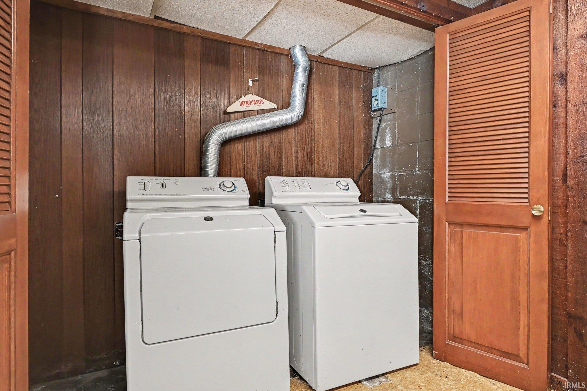 Dedicated laundry area featuring wood paneling, a wood-finish louvered door, exposed concrete block, and a textured ceiling