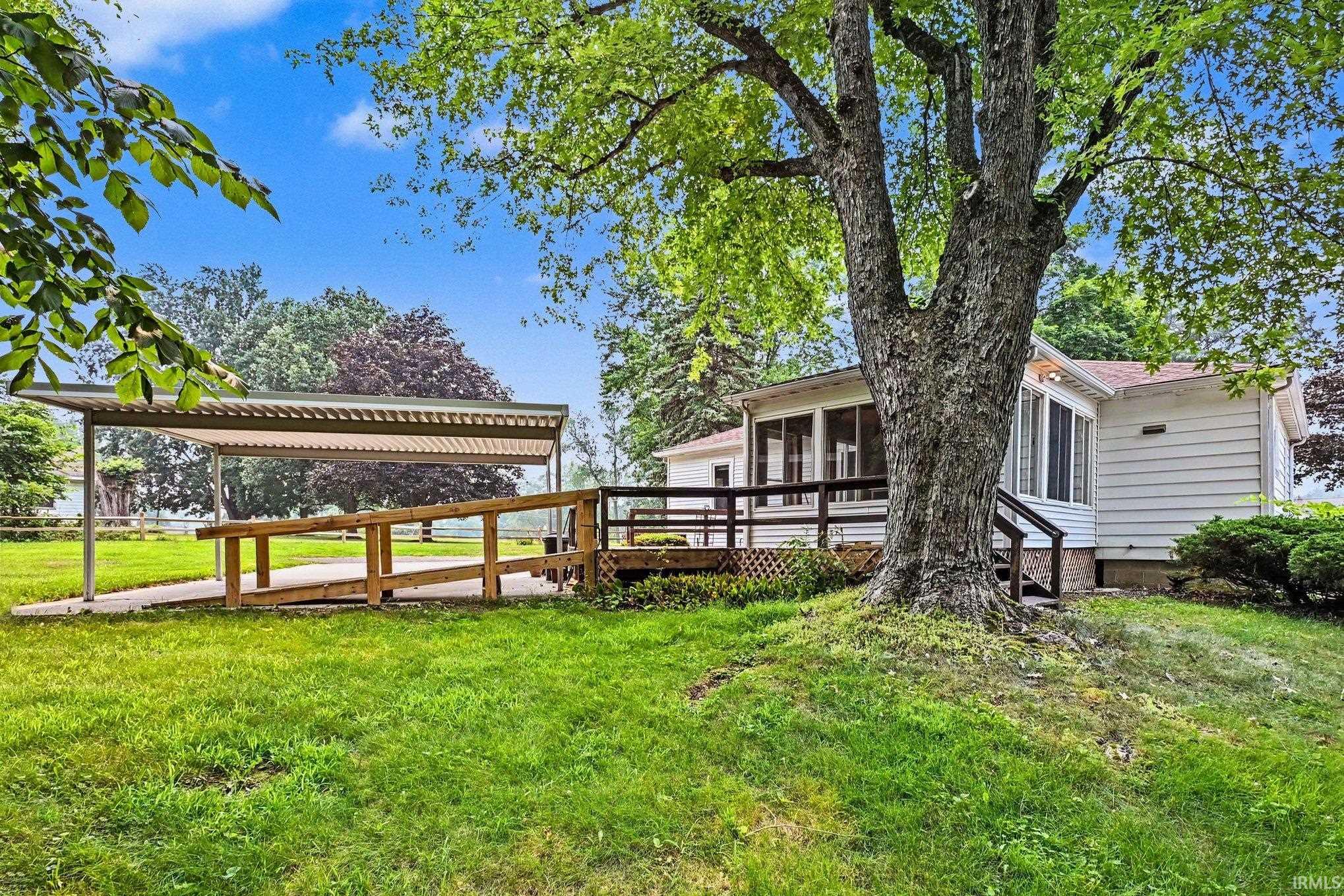 Expansive rear yard featuring a large mature tree, a wood deck with a ramp, and a covered carport structure