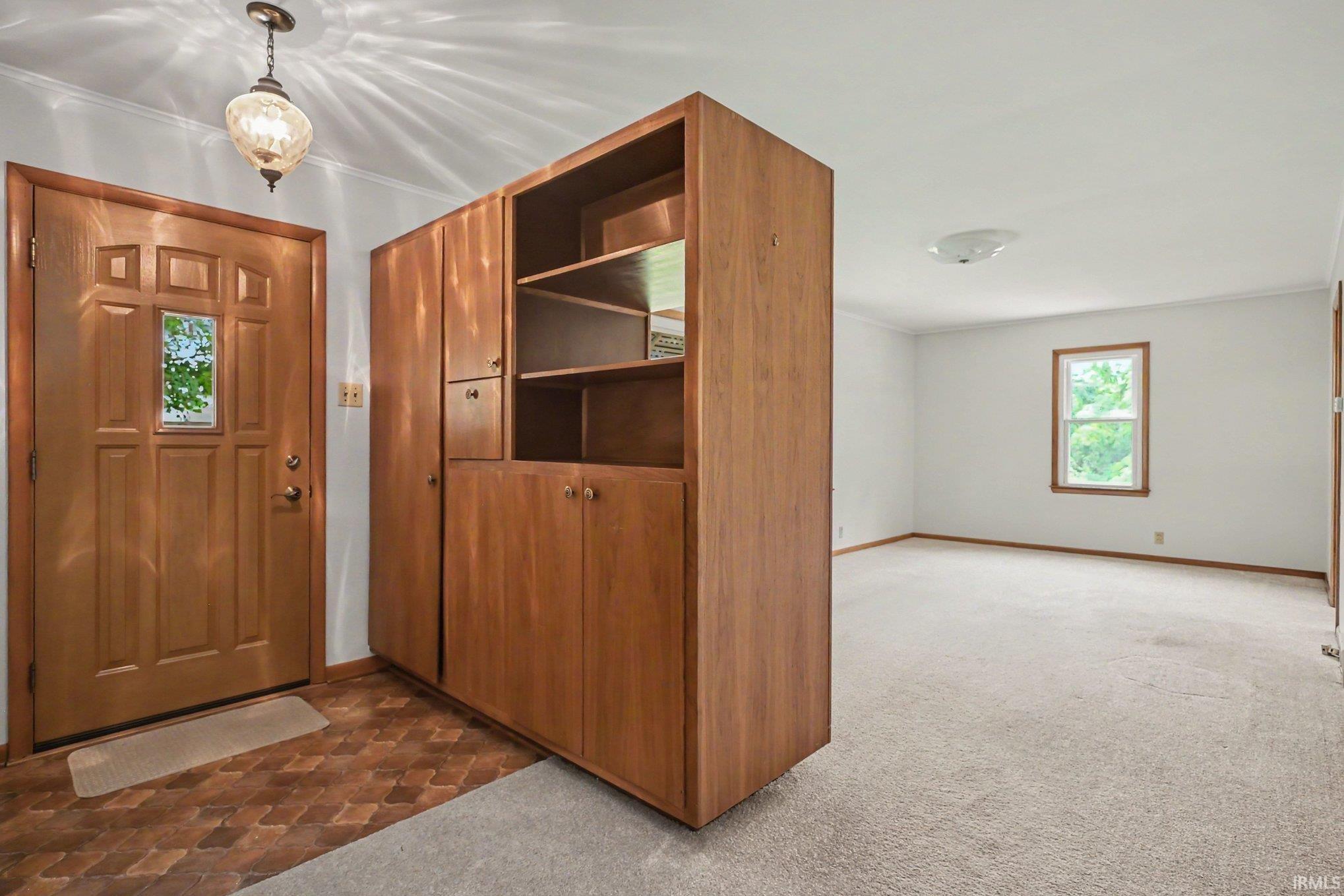 Entryway featuring a paneled wood door with a clear glass insert, a patterned tile-look floor, and a warm wood-finish built-in storage unit with open shelving and cabinet storage