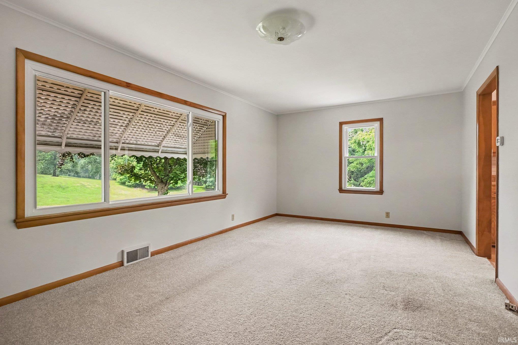 Spacious room featuring light-toned carpeting, white walls, and warm wood trim