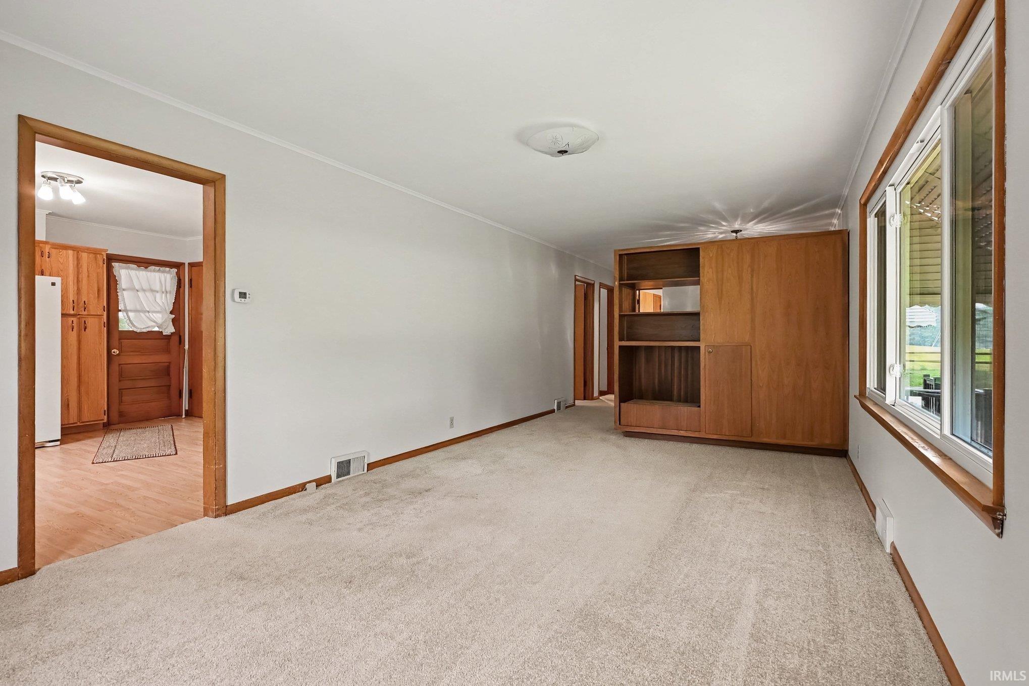Living area featuring light-toned carpeting, white walls, and a built-in wood-finish shelving unit