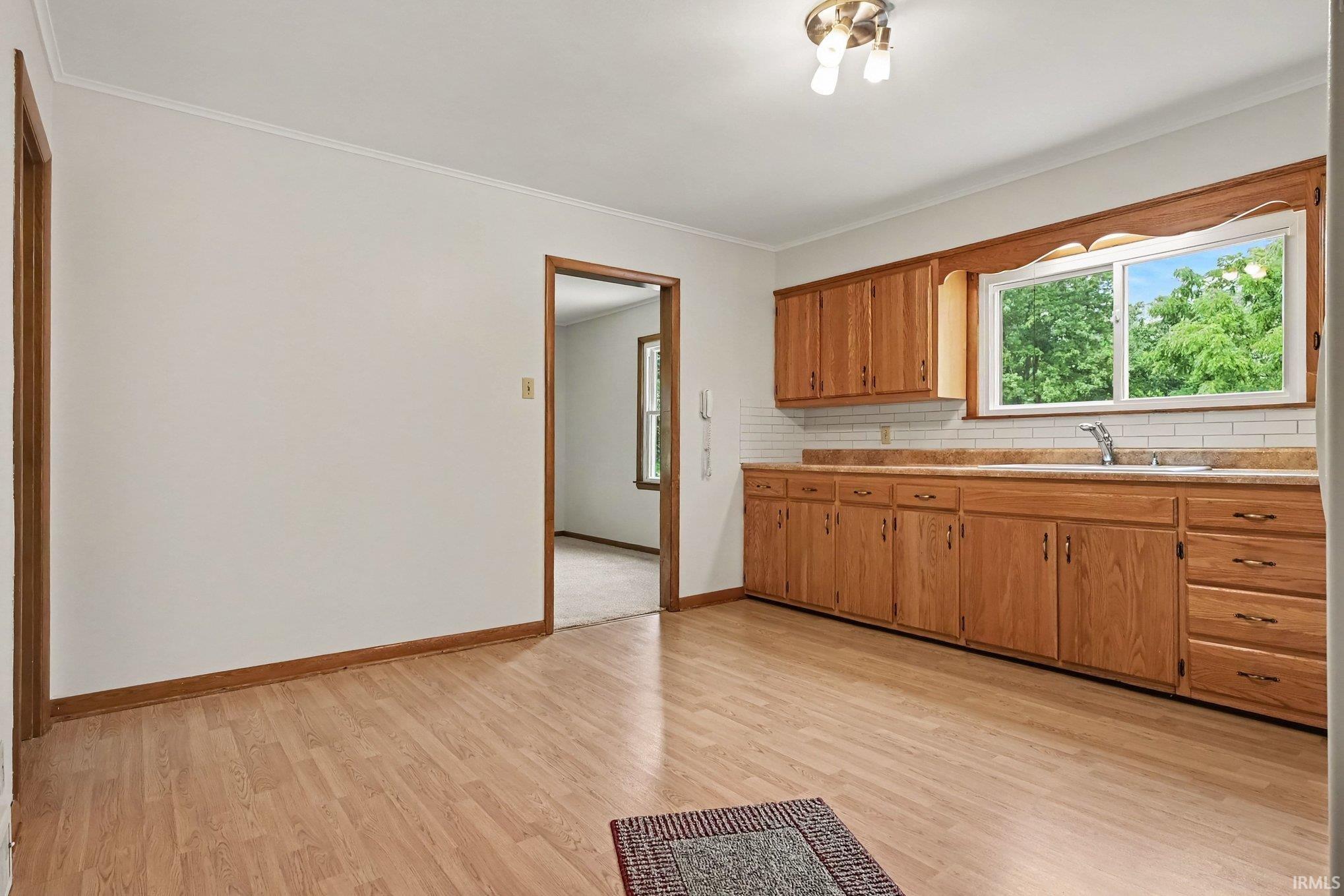 Kitchen featuring wood-finish flooring, natural wood cabinetry, a subway tile backsplash, and a double-pane window