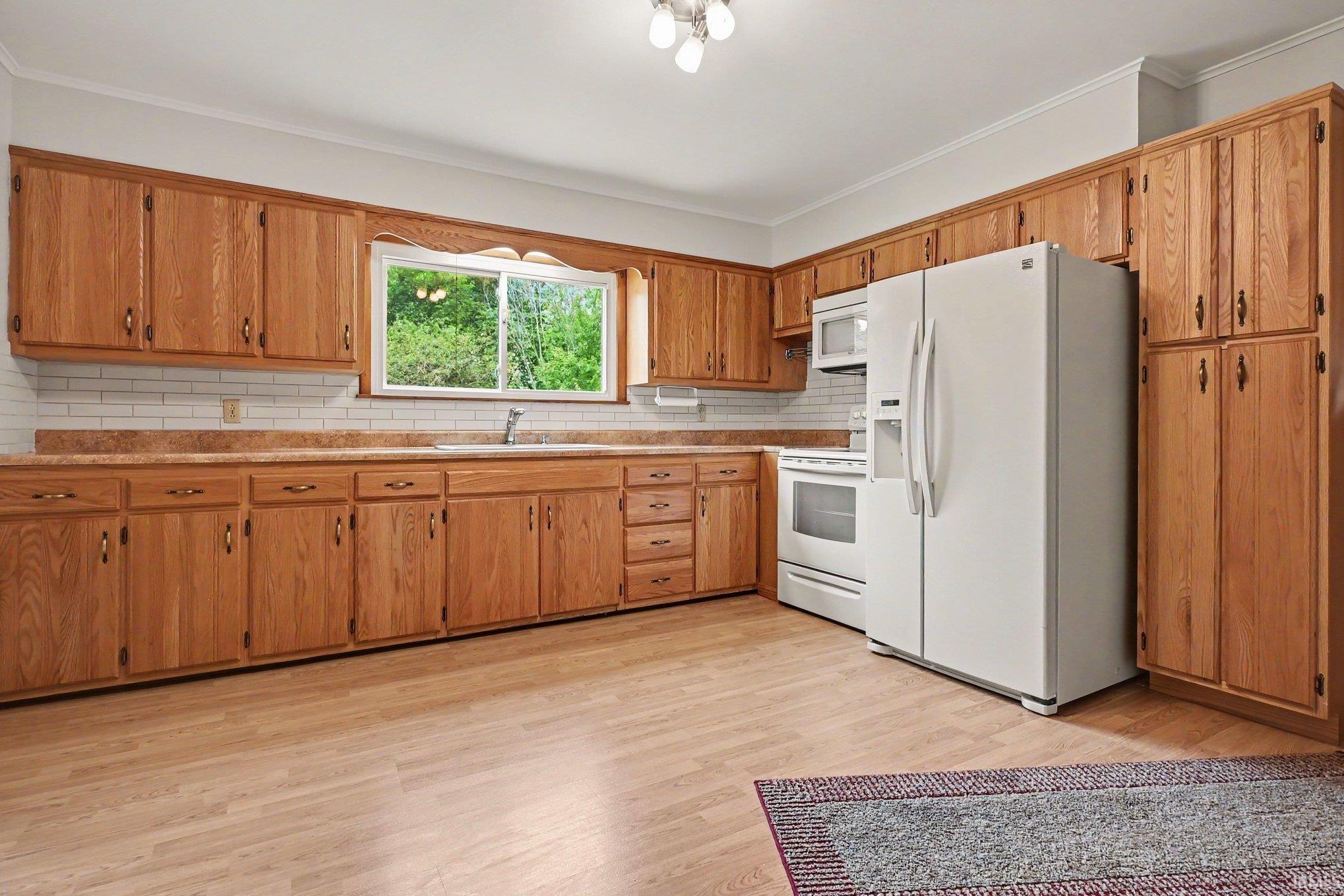 Kitchen featuring extensive wood cabinetry, white subway tile backsplash, and light wood-finish flooring