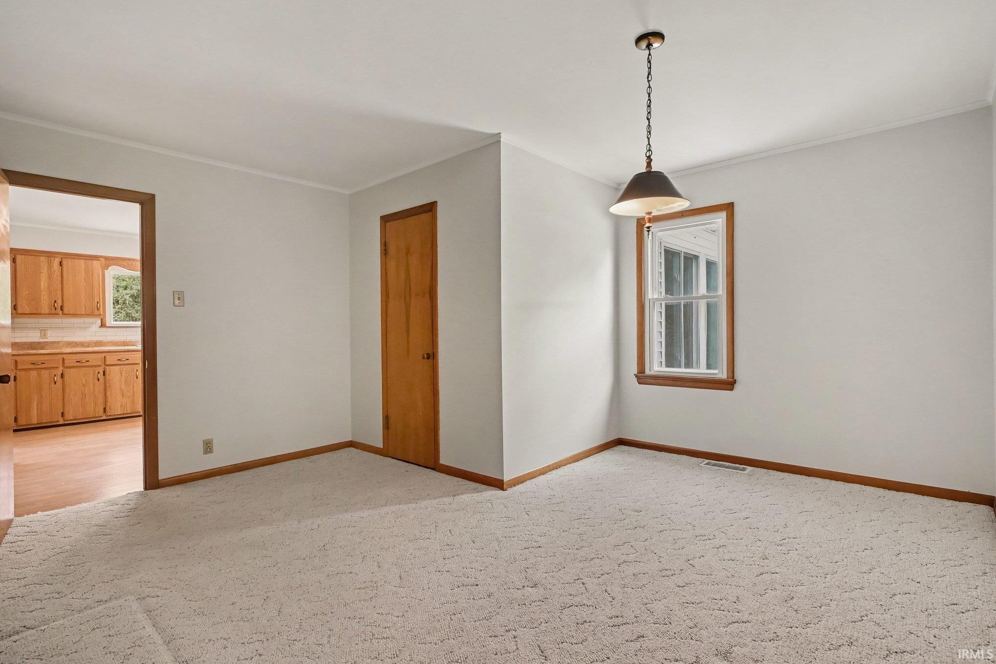 Carpeted room with a ceiling-mounted light fixture, a window with wood trim, and a wood door